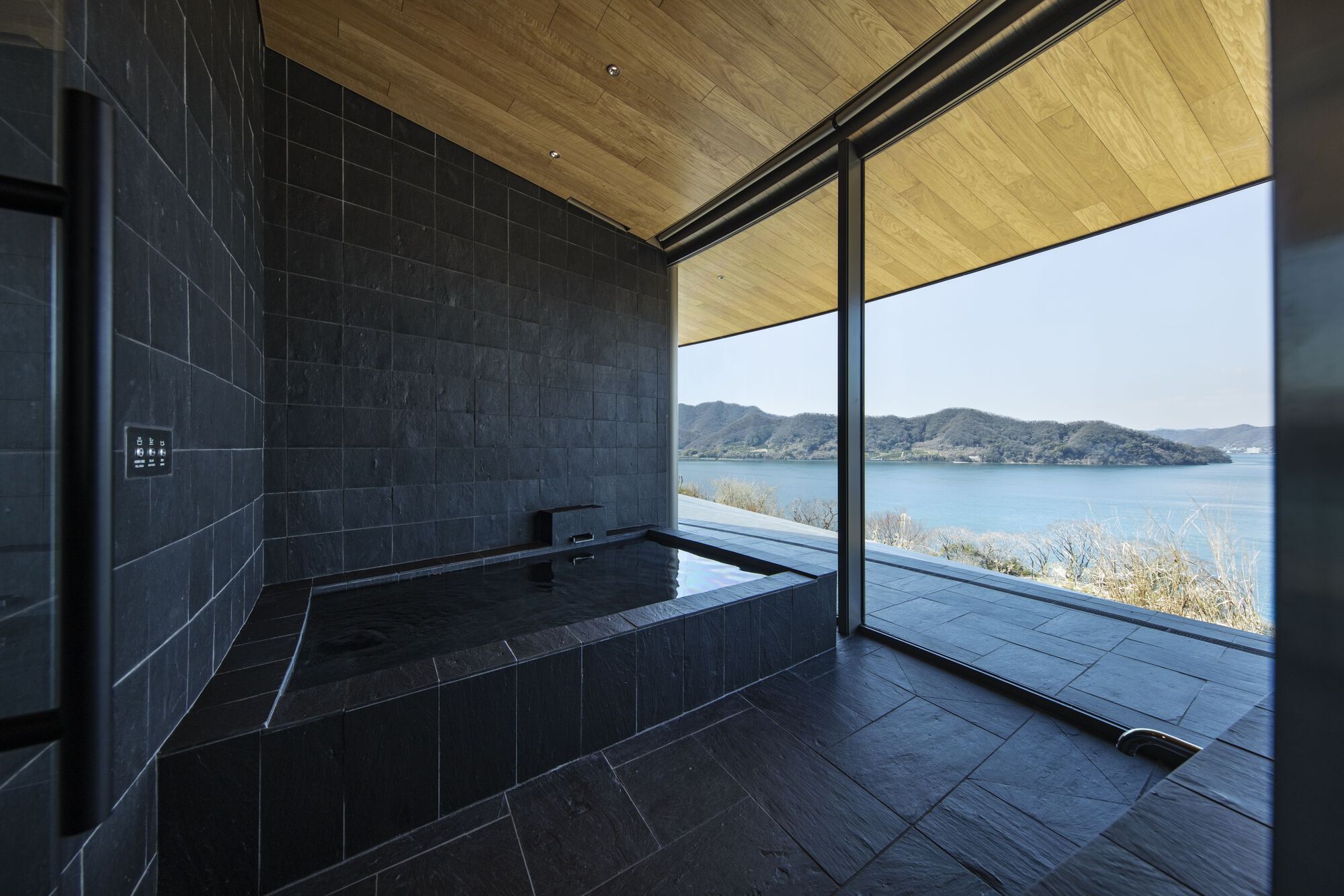 Tiled soaking tub with glazed wall overlooking coastal grasses and the lake beyond
