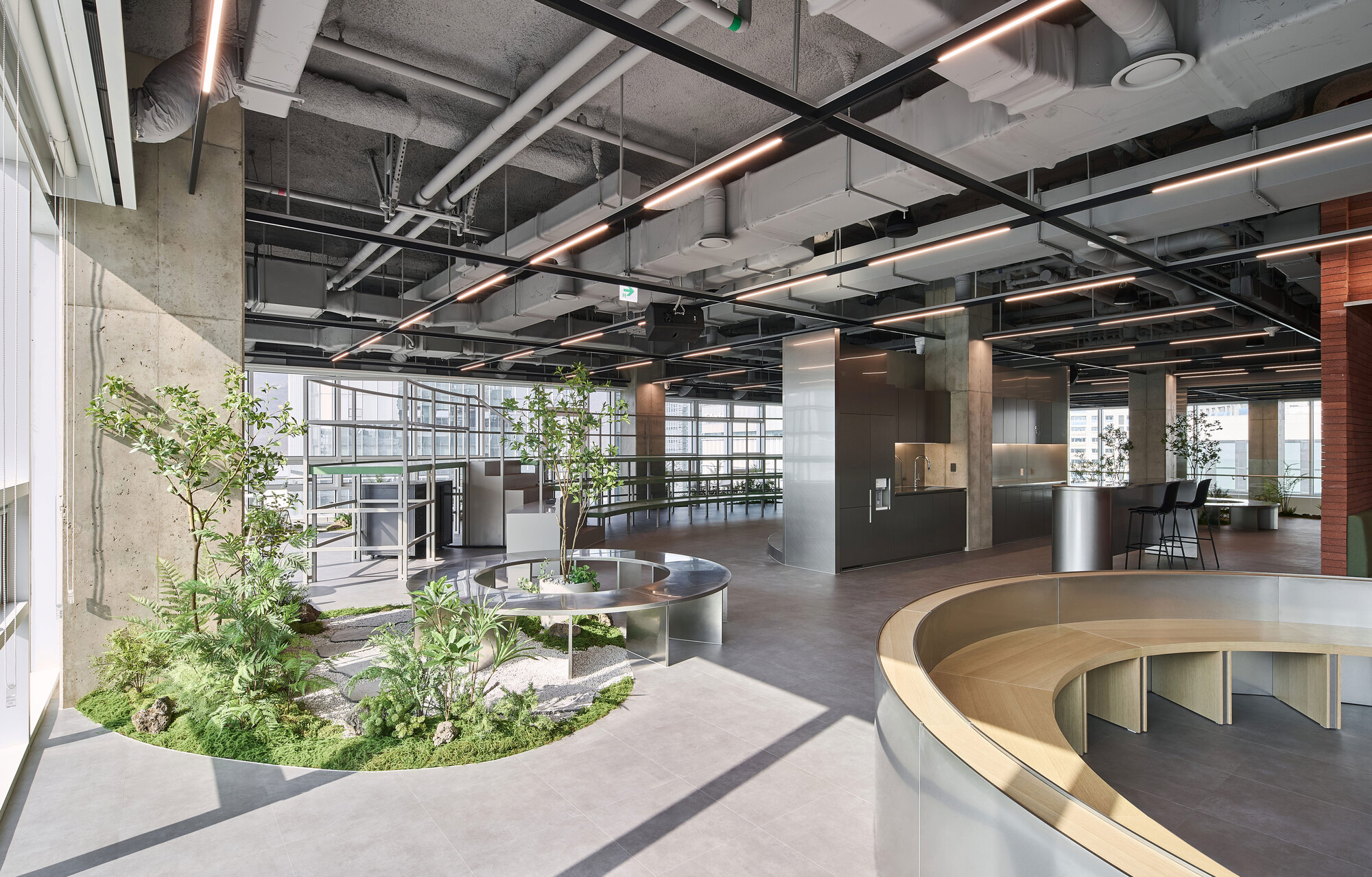 Open office floor with circular glass balustrade overlooking an interior planted courtyard beneath exposed ceiling systems