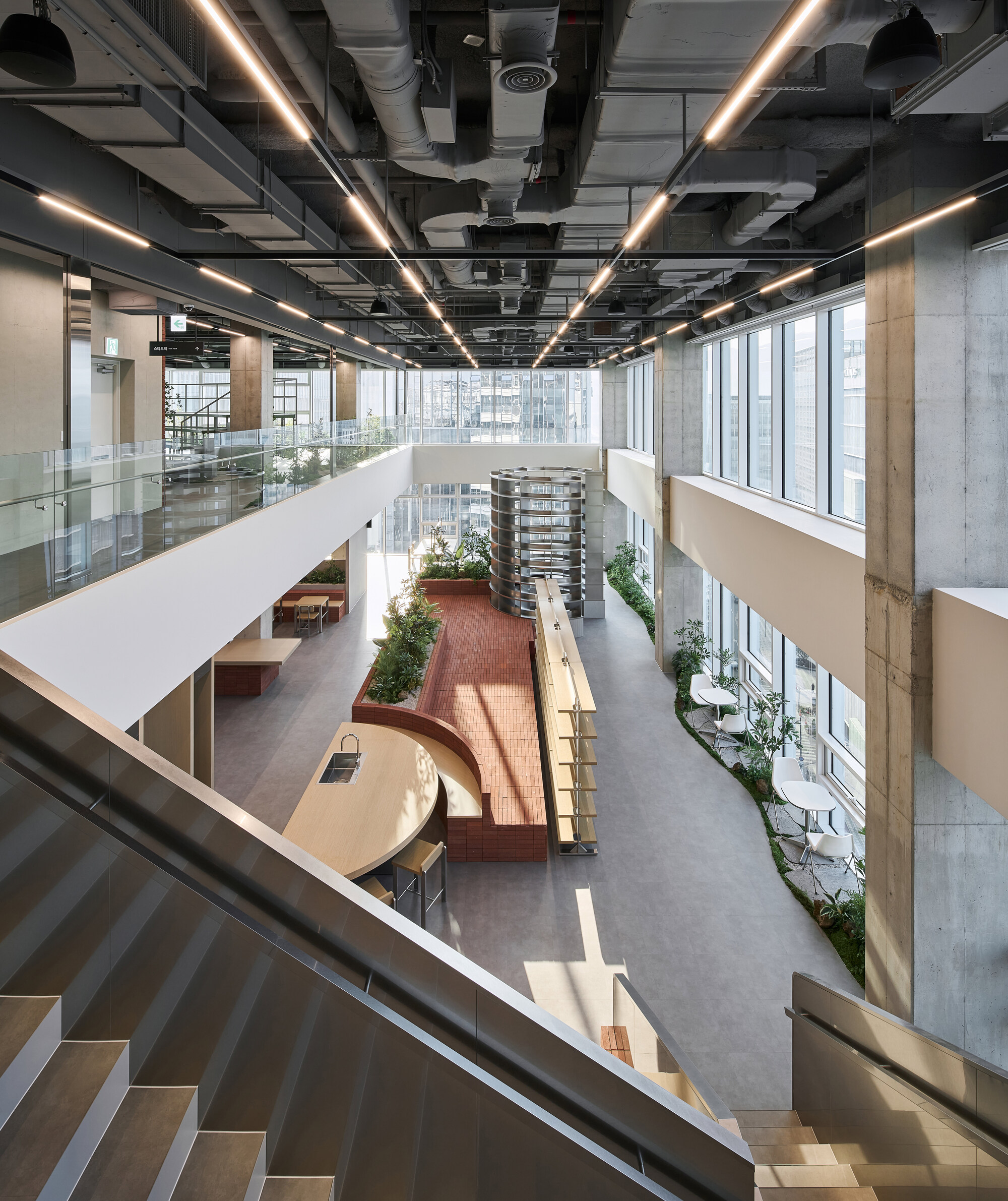 View from upper level staircase down to the atrium with terracotta seating platforms and planted beds