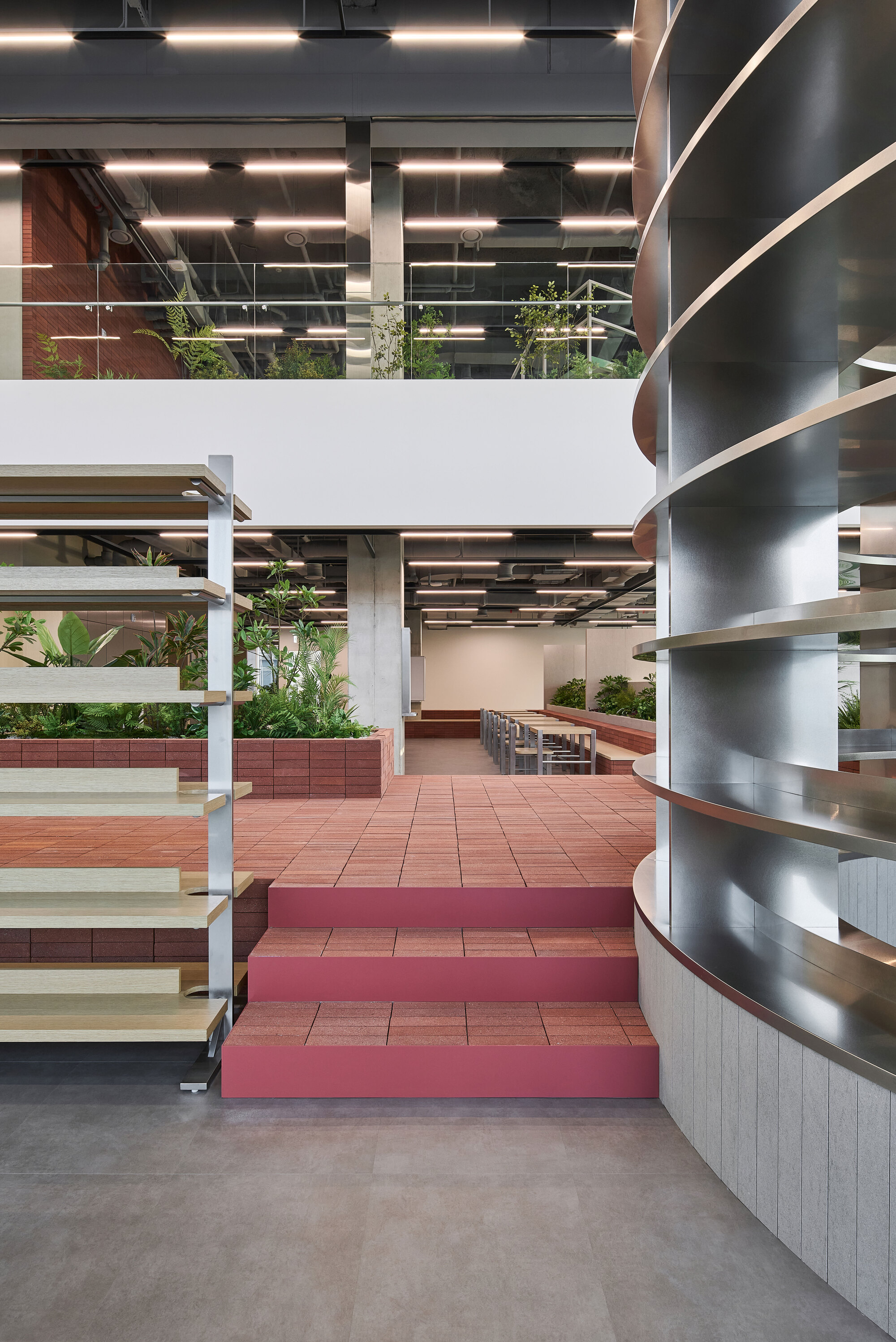 Tiered seating platforms in terracotta and burgundy tiles ascending toward white open-riser shelving units
