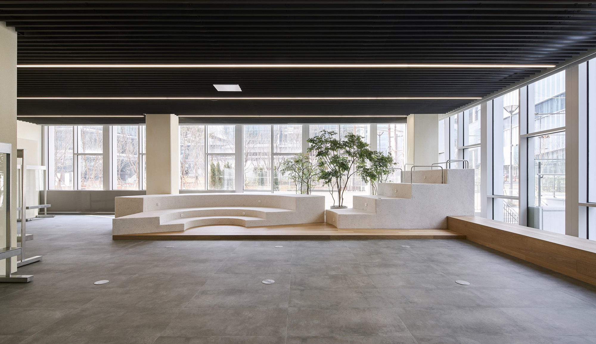 Curved white concrete seating plinth beside floor-to-ceiling windows under a black slatted ceiling