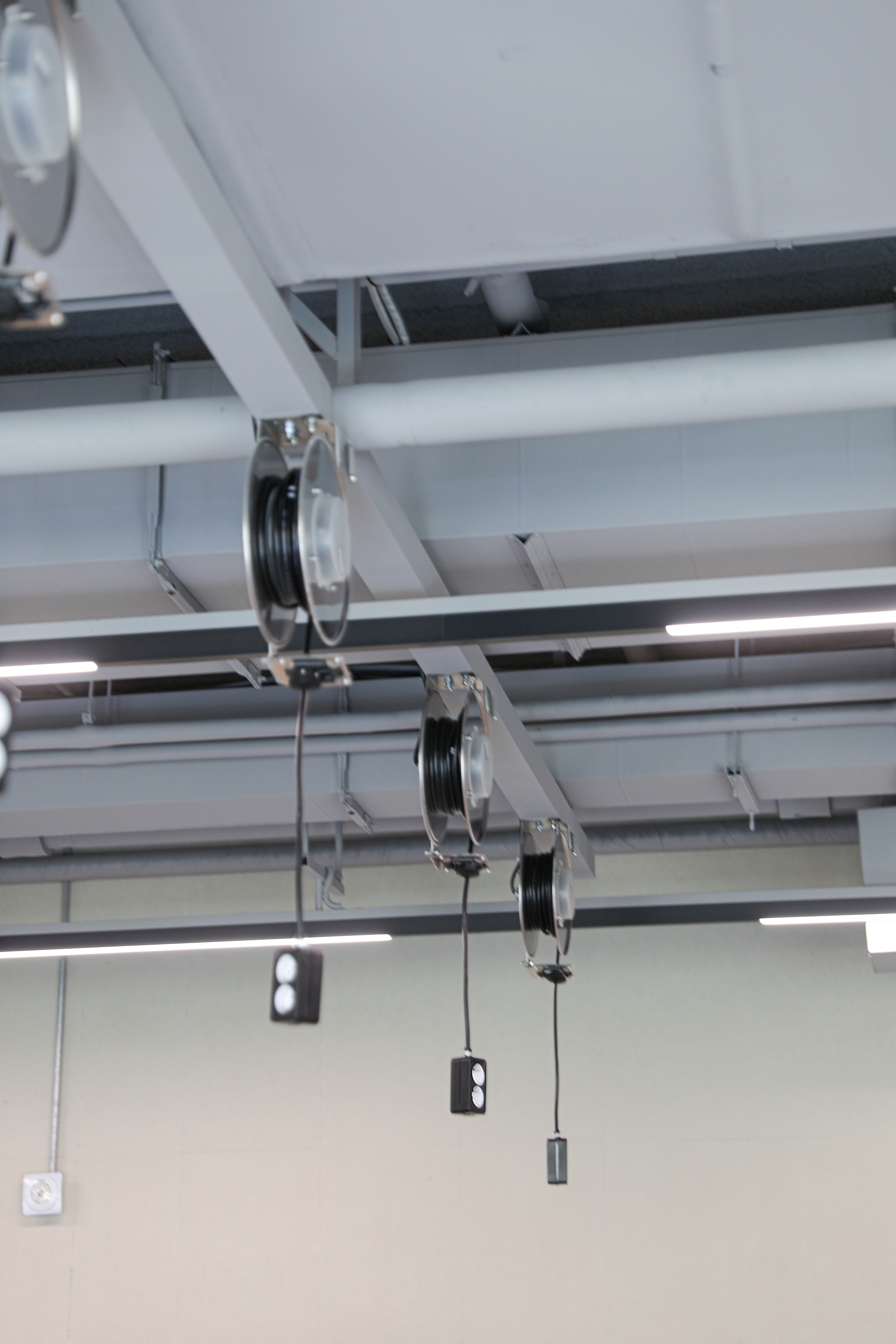 Close-up of ceiling pulley system with steel cables and pendant weights beneath linear light fixtures