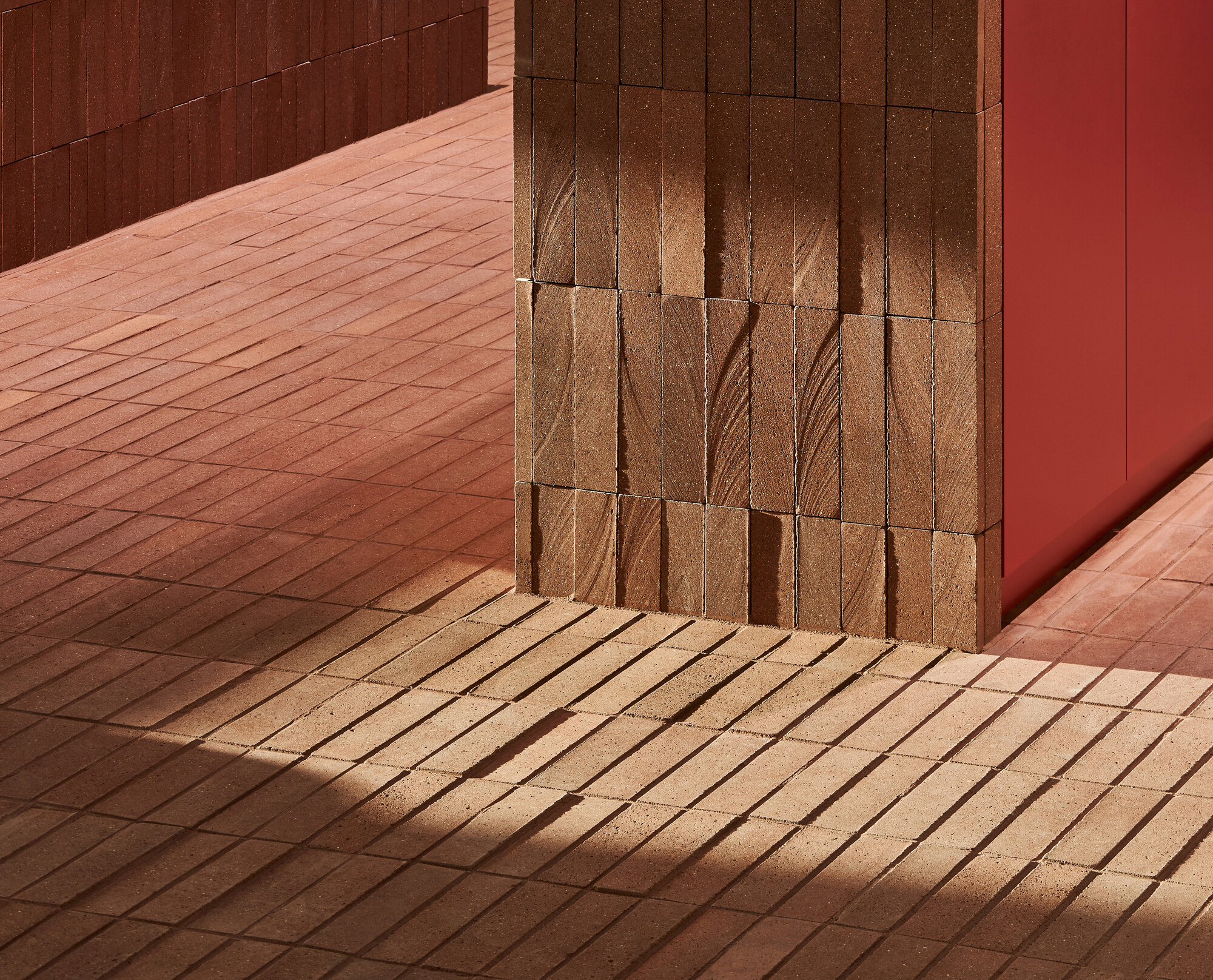Textured terracotta tile column and floor meeting a red wall in direct sunlight