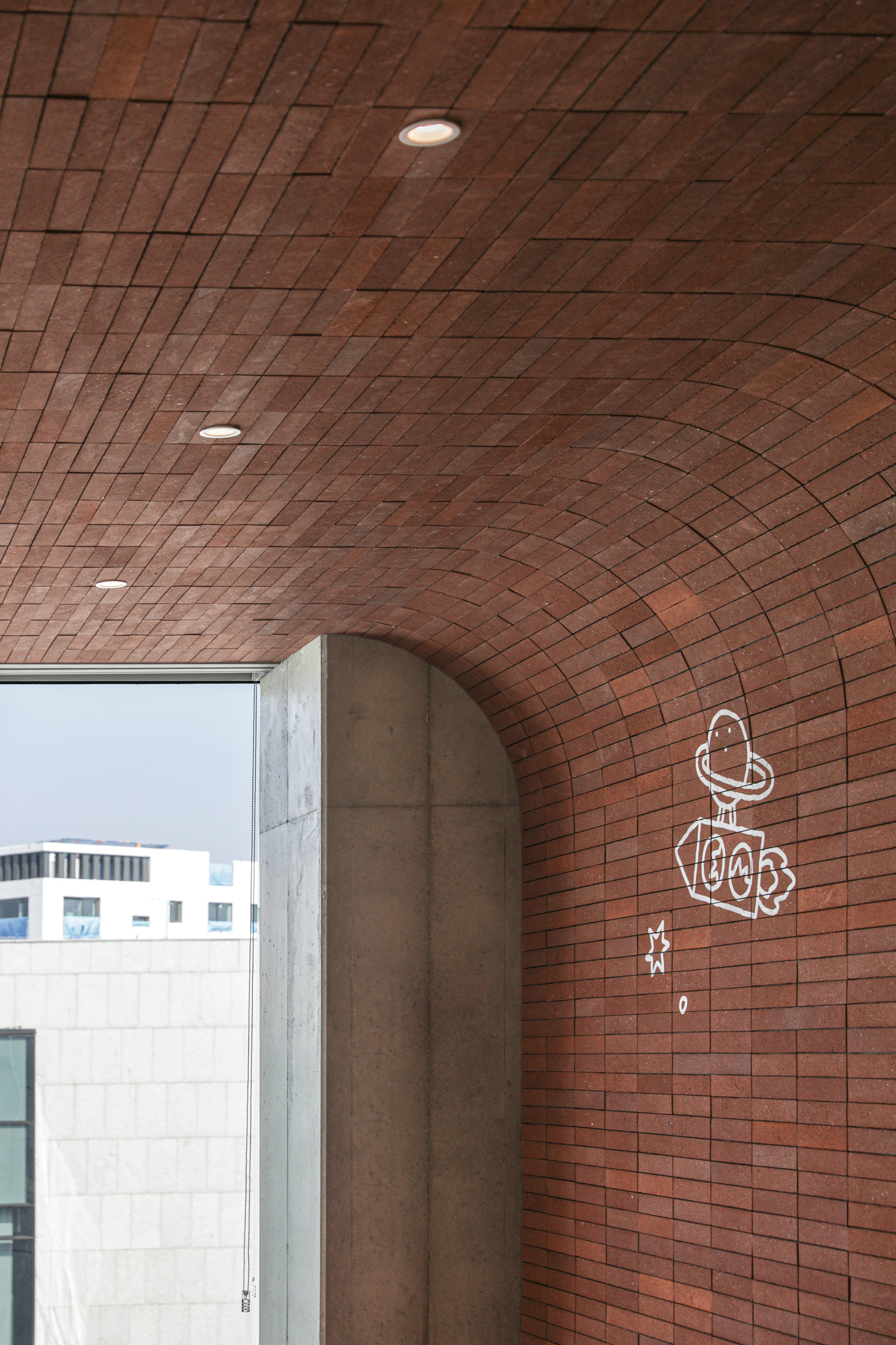 Vaulted red tile ceiling with recessed lights and concrete column framing an exterior view