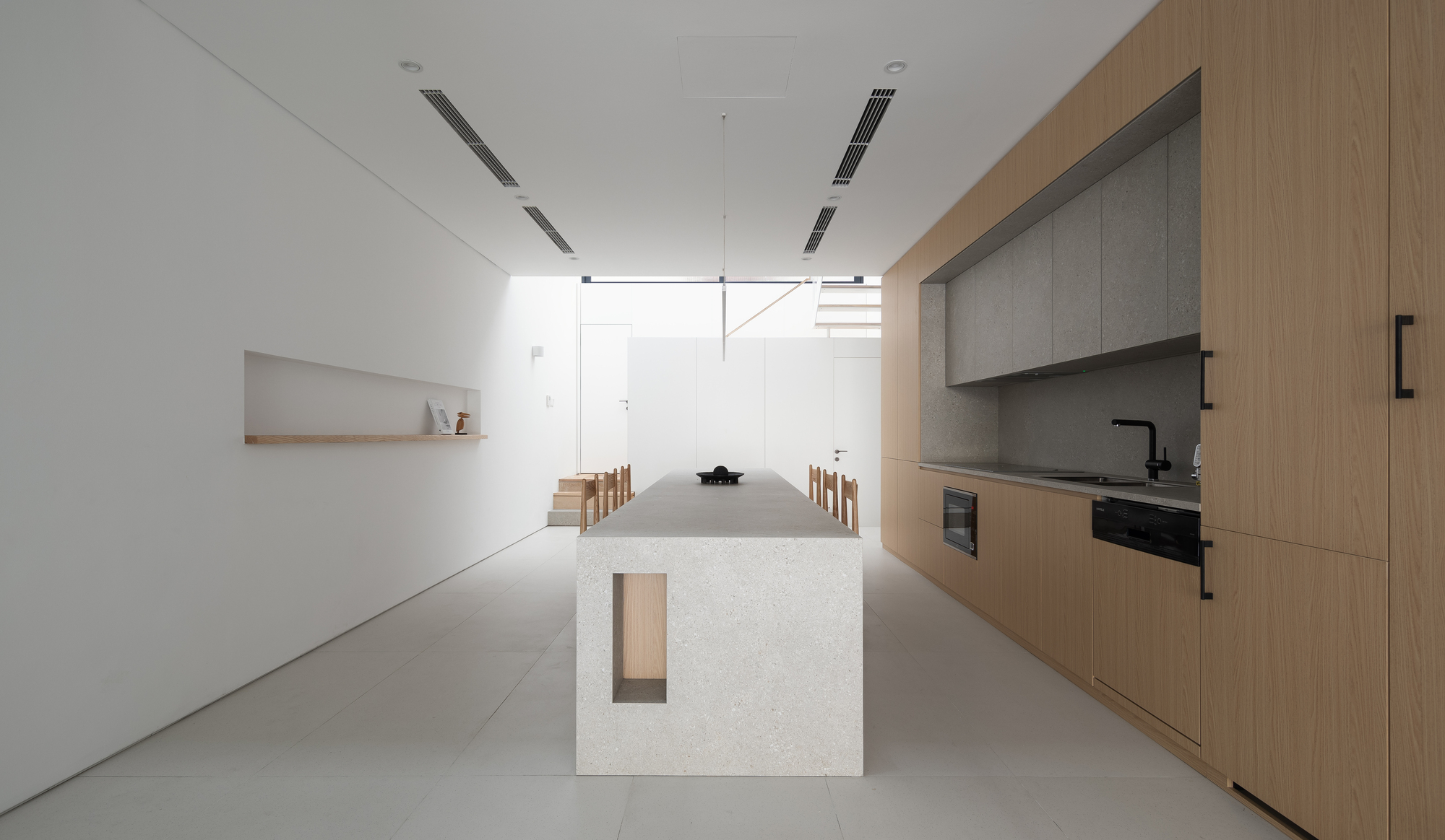 Open kitchen and dining area with a terrazzo island, timber cabinetry, and white walls under linear ceiling fixtures