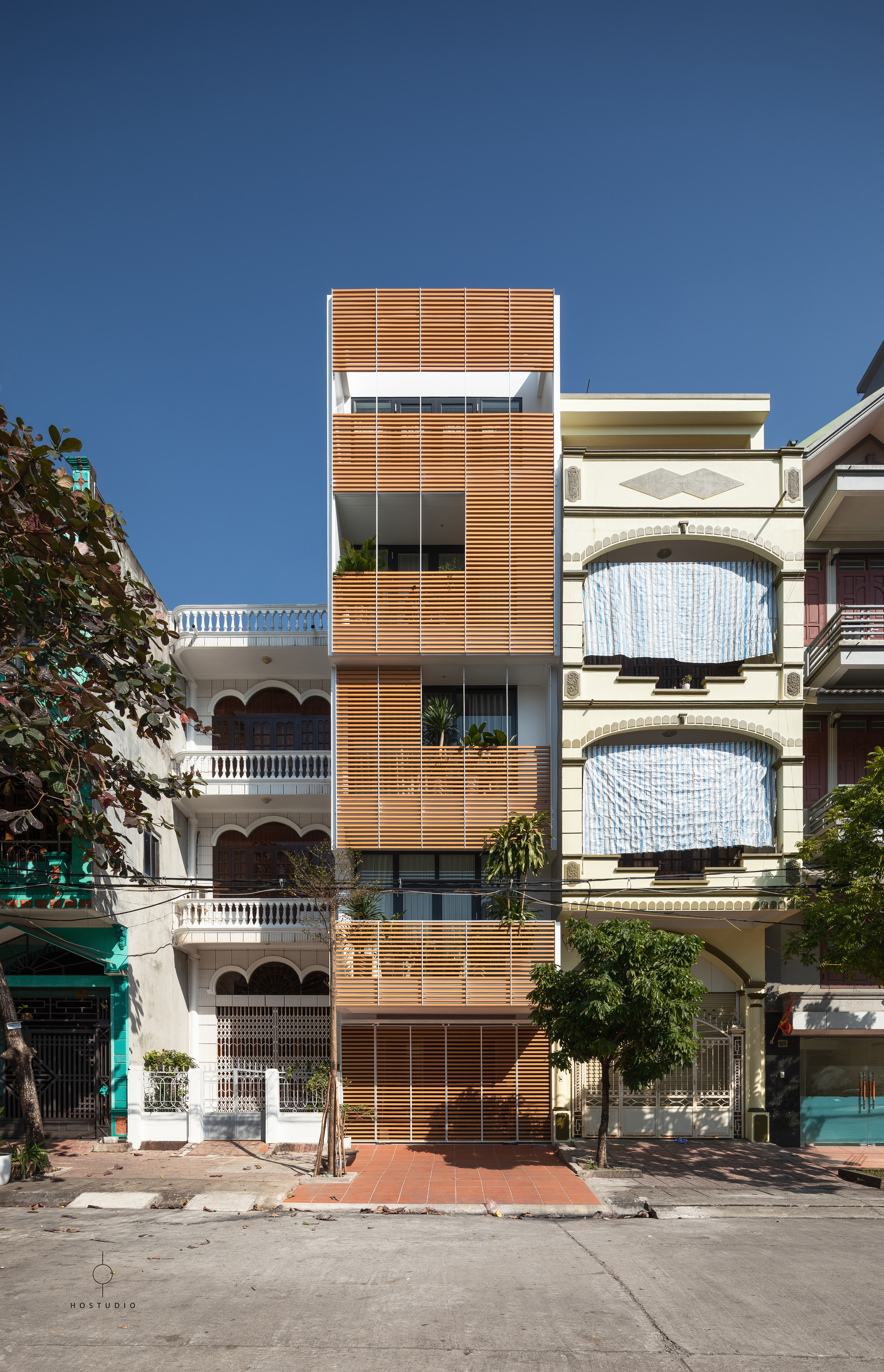 Front elevation of the narrow tower with timber screens between neighboring buildings on a residential street
