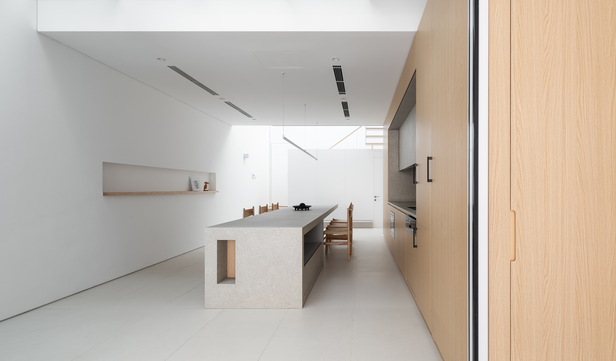 Long view of the kitchen island with light wood cabinetry and pale tile flooring