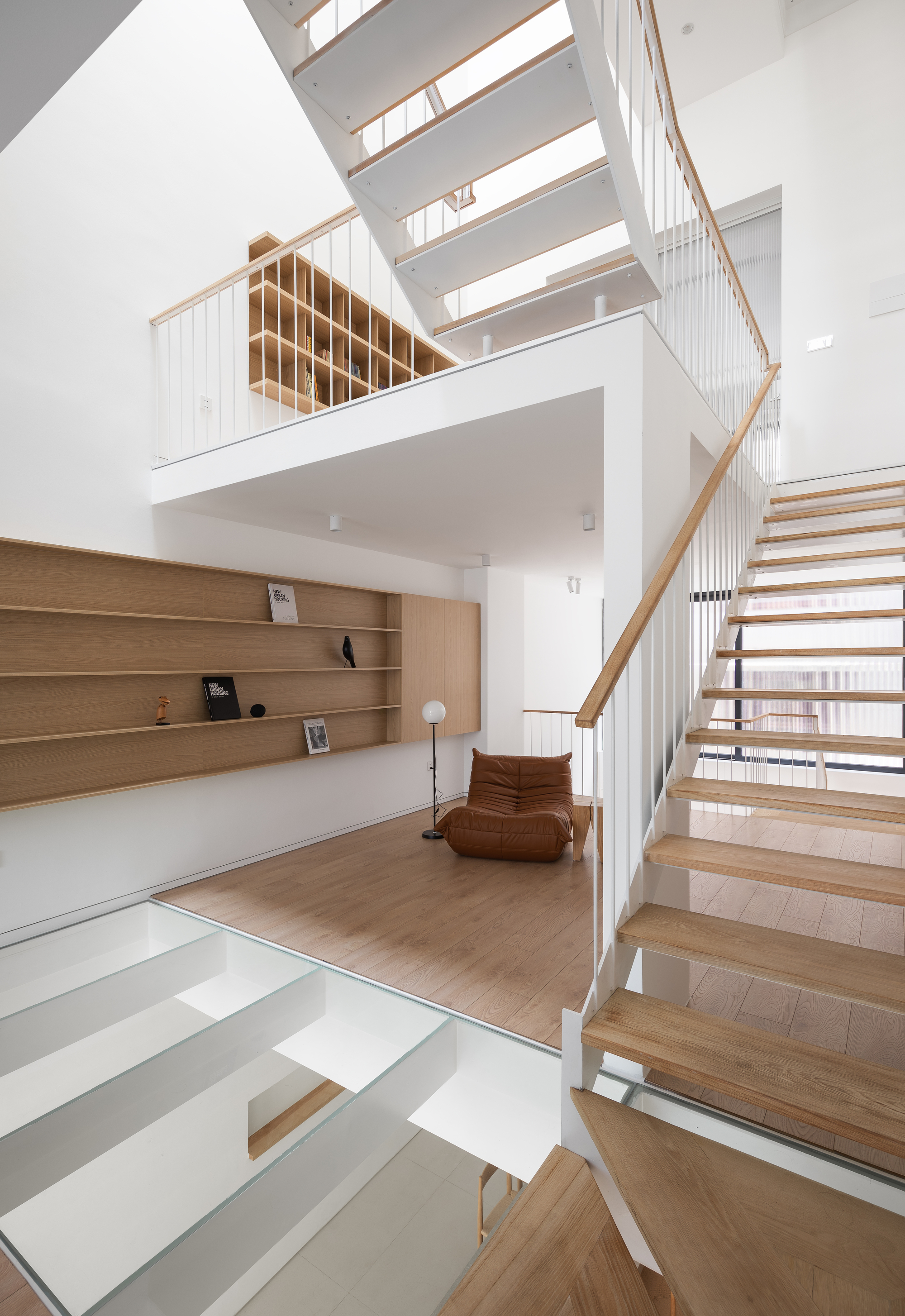 Double-height living space with timber staircase and shelving under skylights casting midday shadows