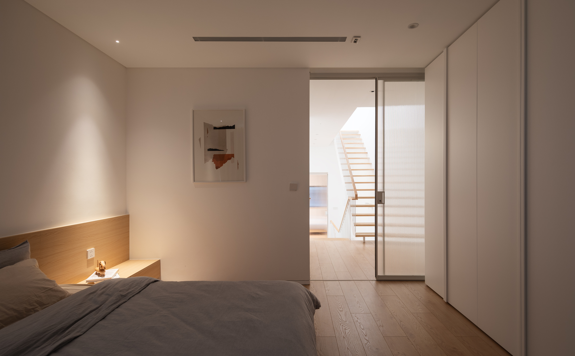 Bedroom with glass sliding door opening to hallway and floating staircase at dusk