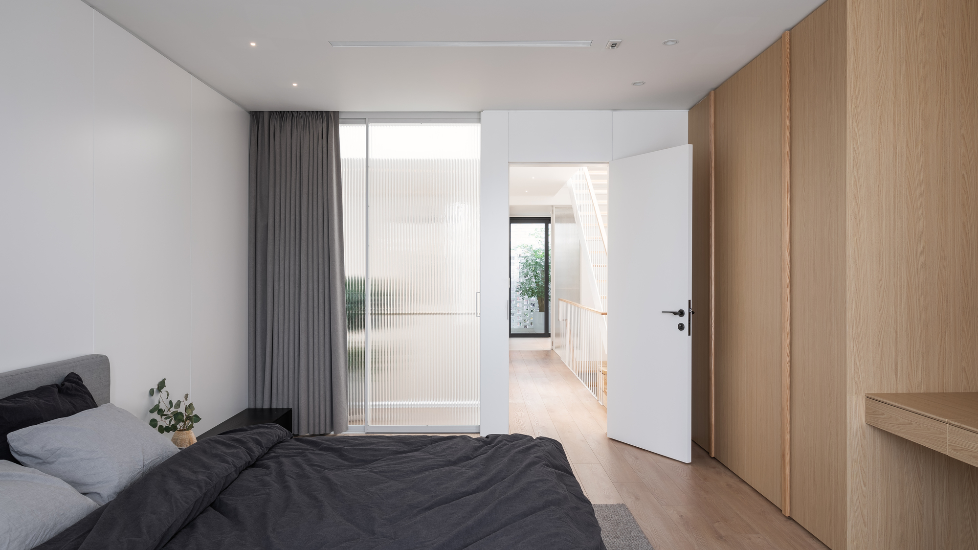 Bedroom with translucent glass partition and view through doorway to planted courtyard beyond