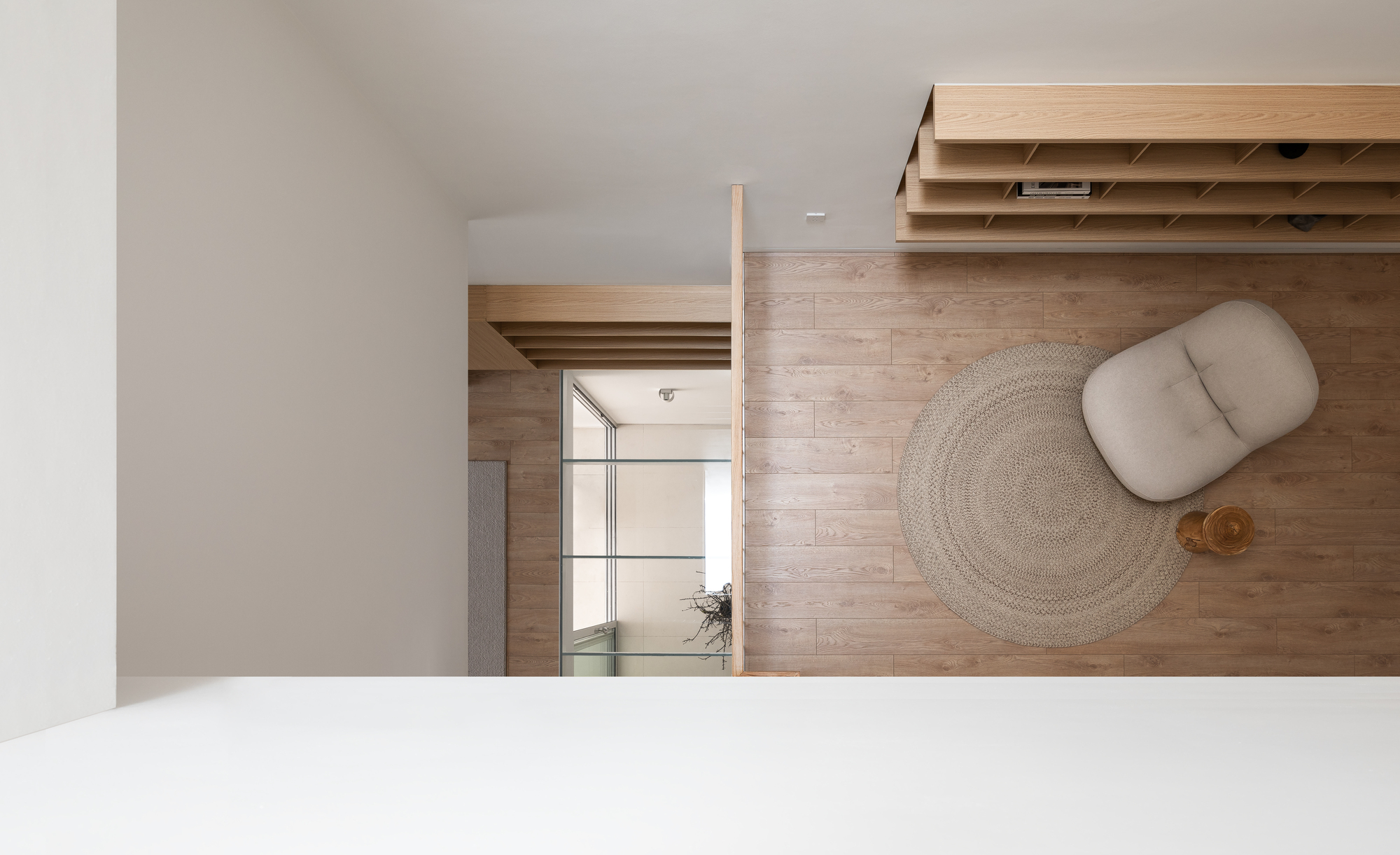 Overhead view of timber flooring with a woven rug and cushion beneath a timber storage unit