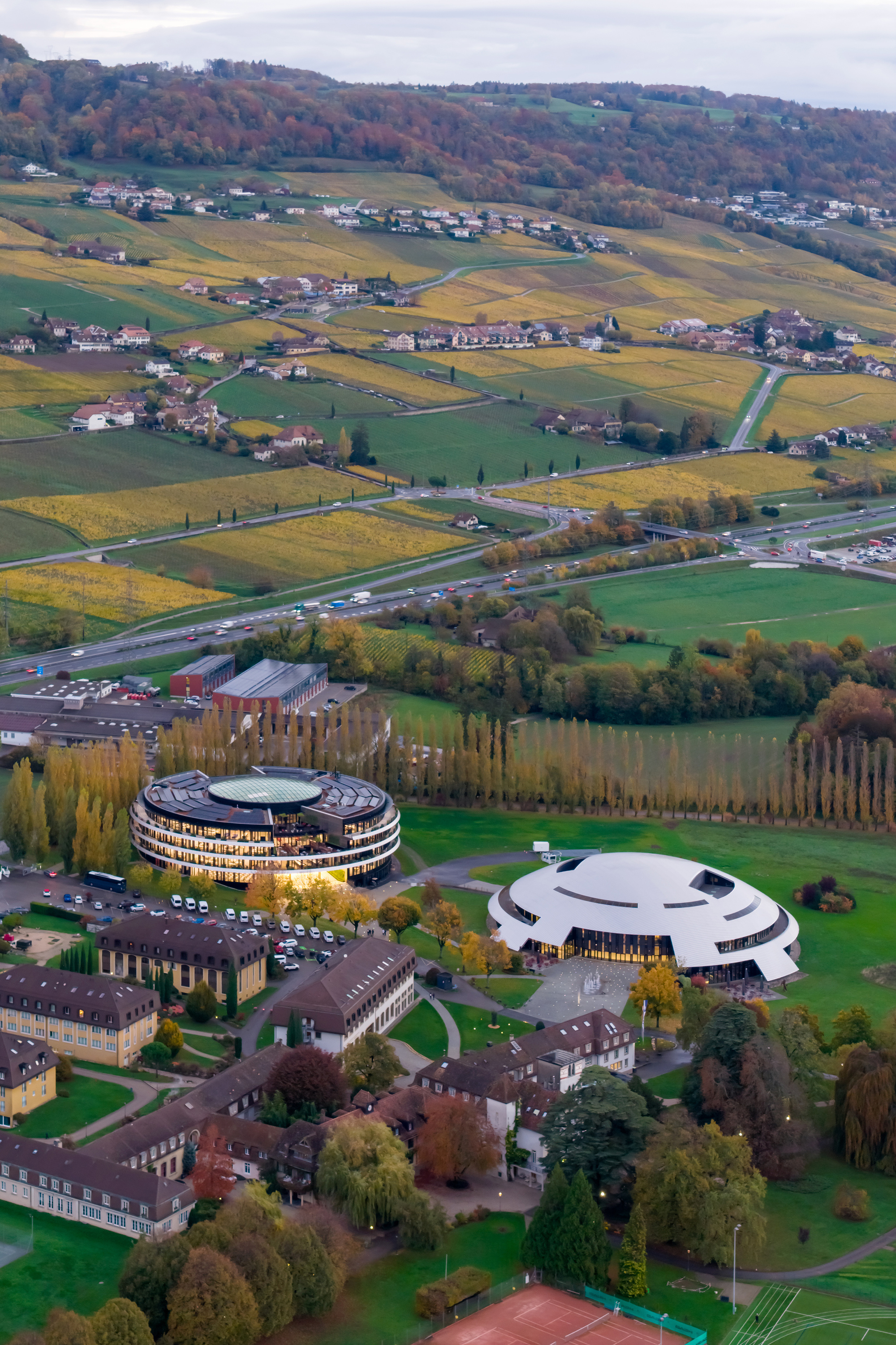 Aerial view of two circular buildings and a white disc-shaped structure among autumn fields