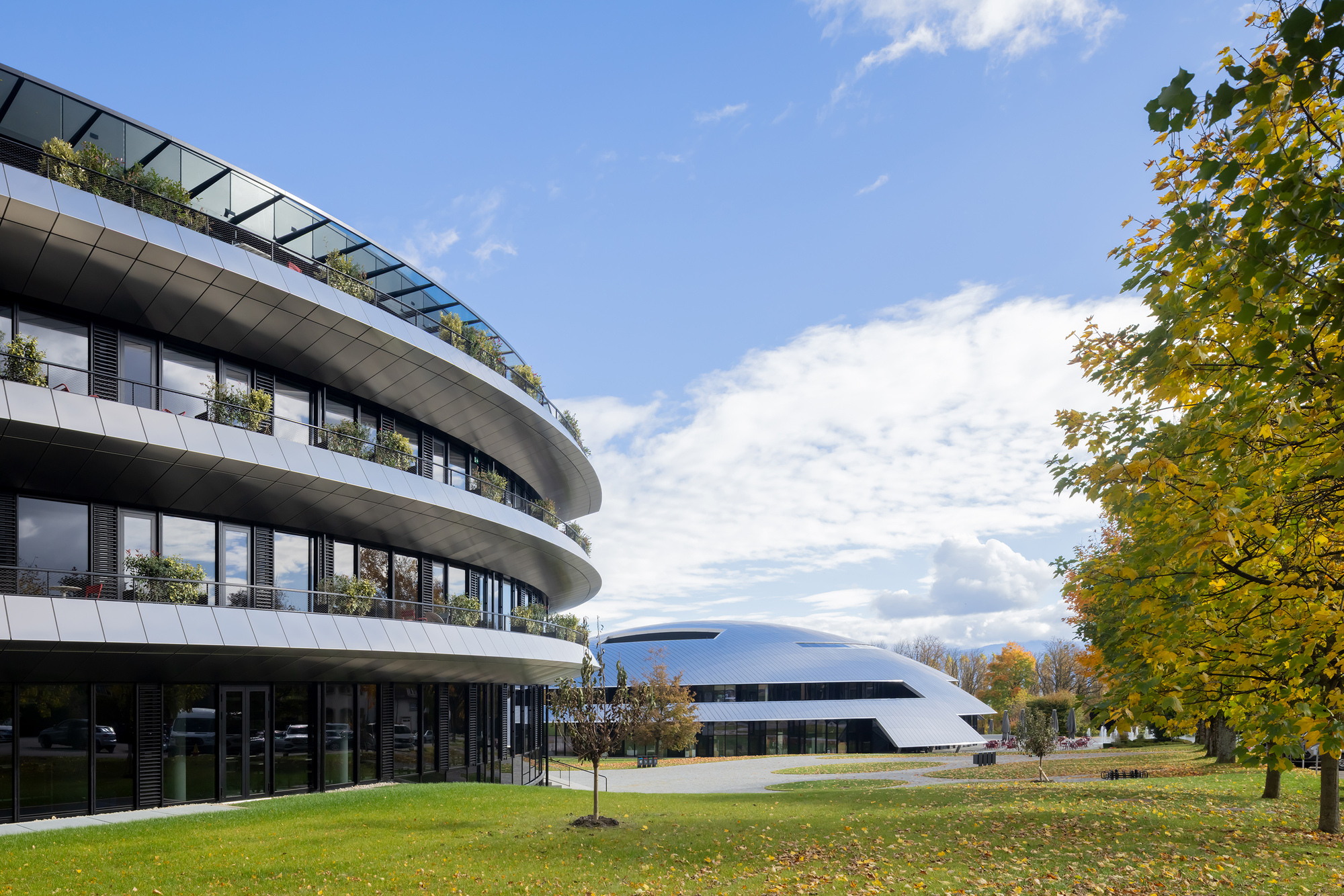 Planted rooftop terrace above curving balconies facing a white disc building across the lawn