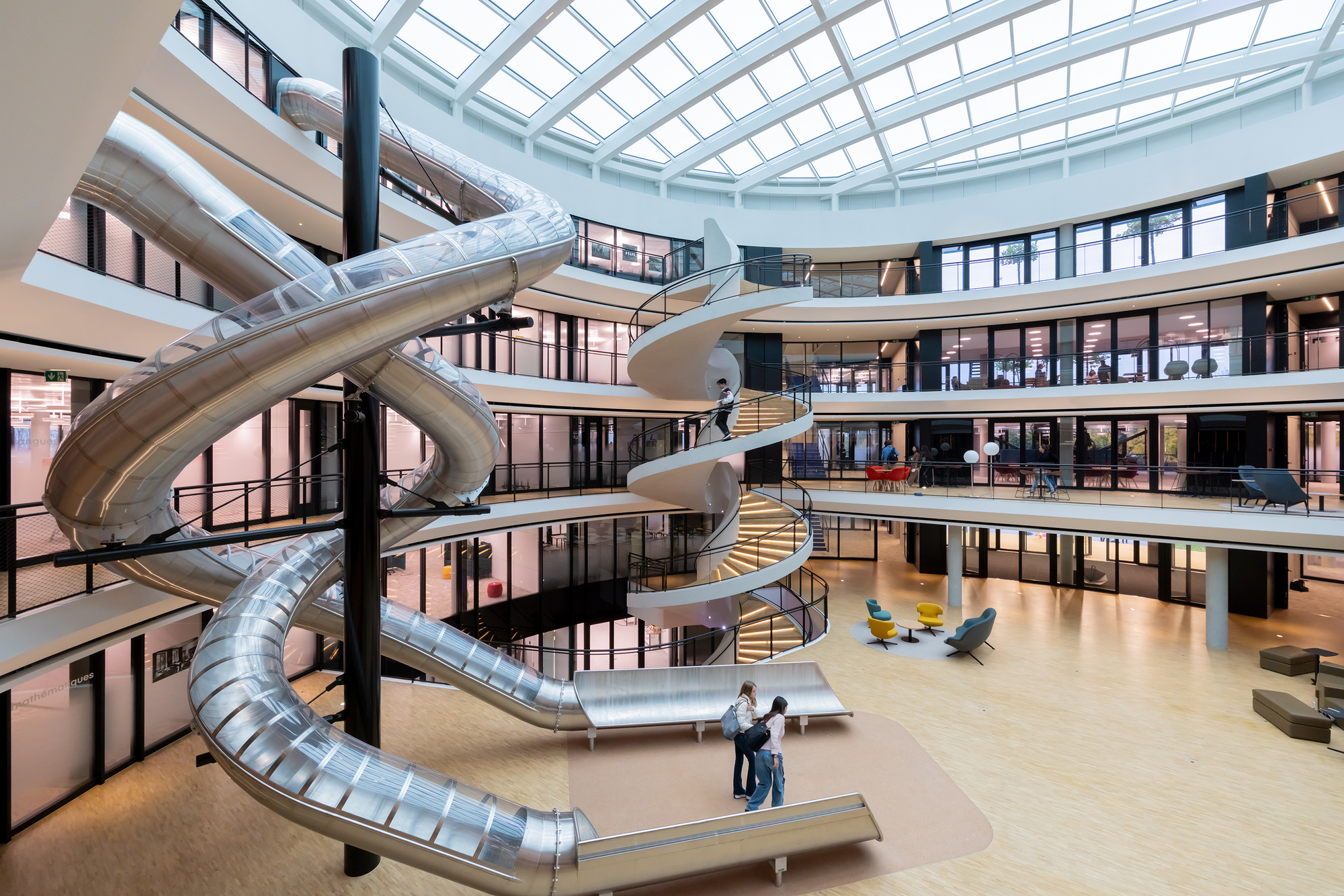 Metallic tubular slide winding through the multi-story atrium with two figures below