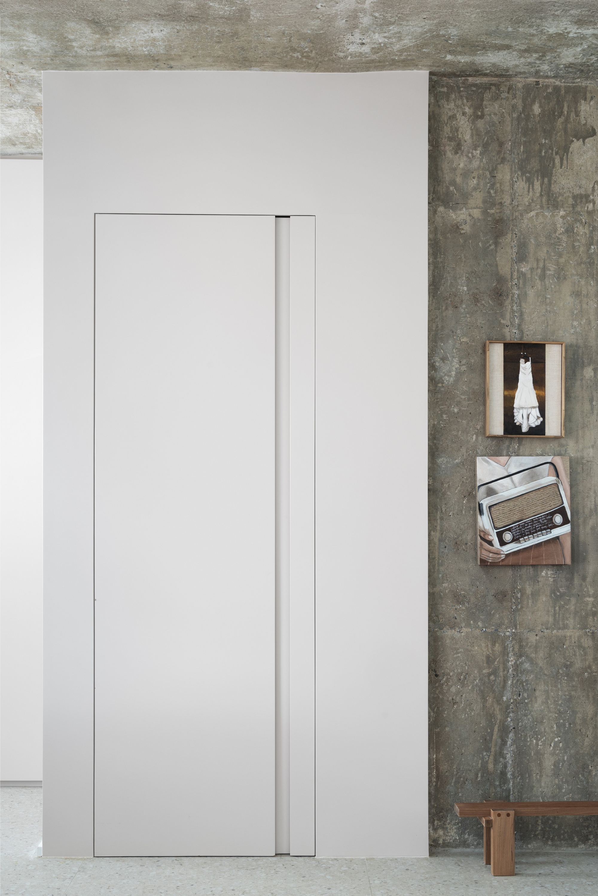 Flush white pocket door beside exposed concrete wall with wooden shelves and a vintage radio