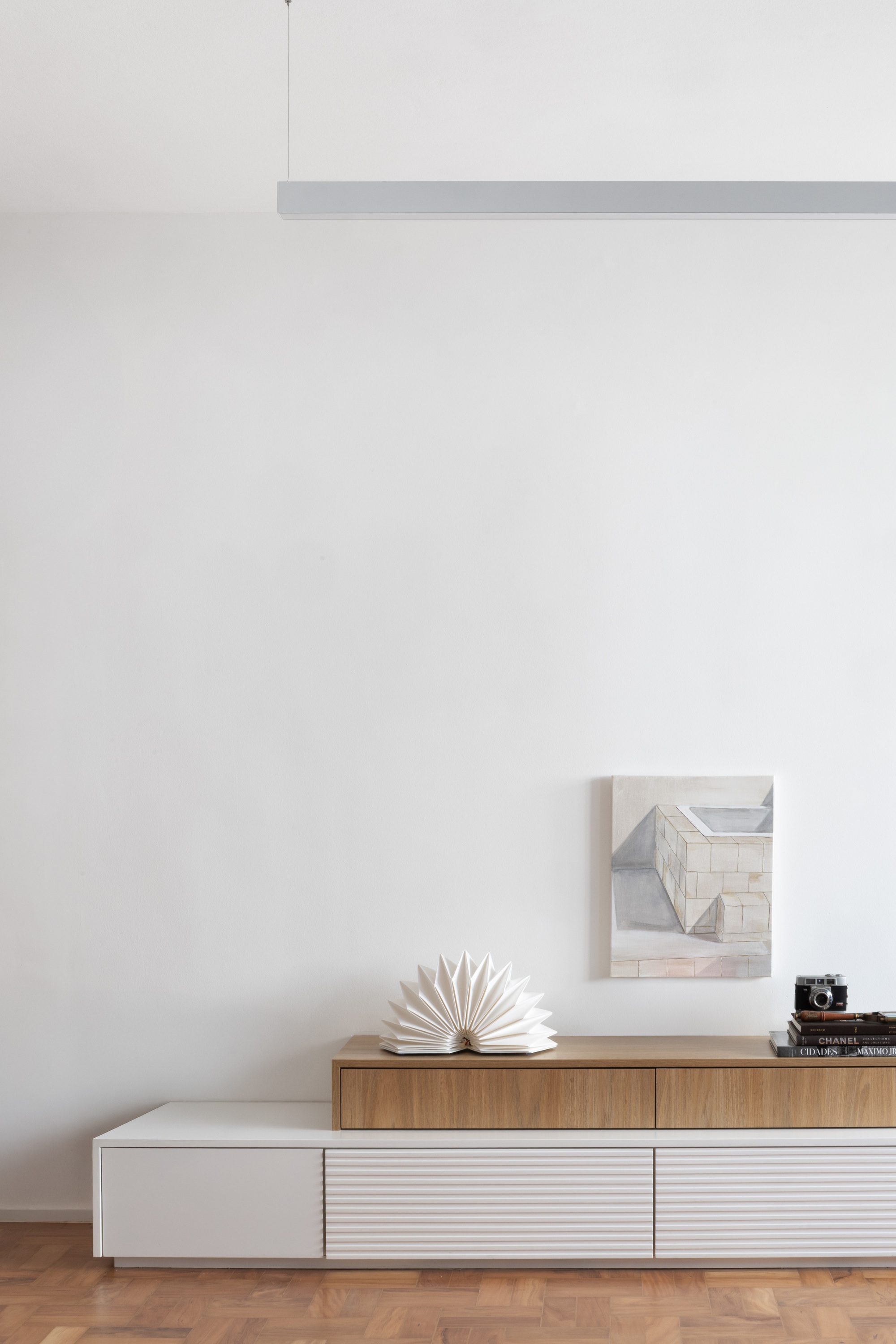 Low storage unit with timber and white panels beneath a white wall with pendant light