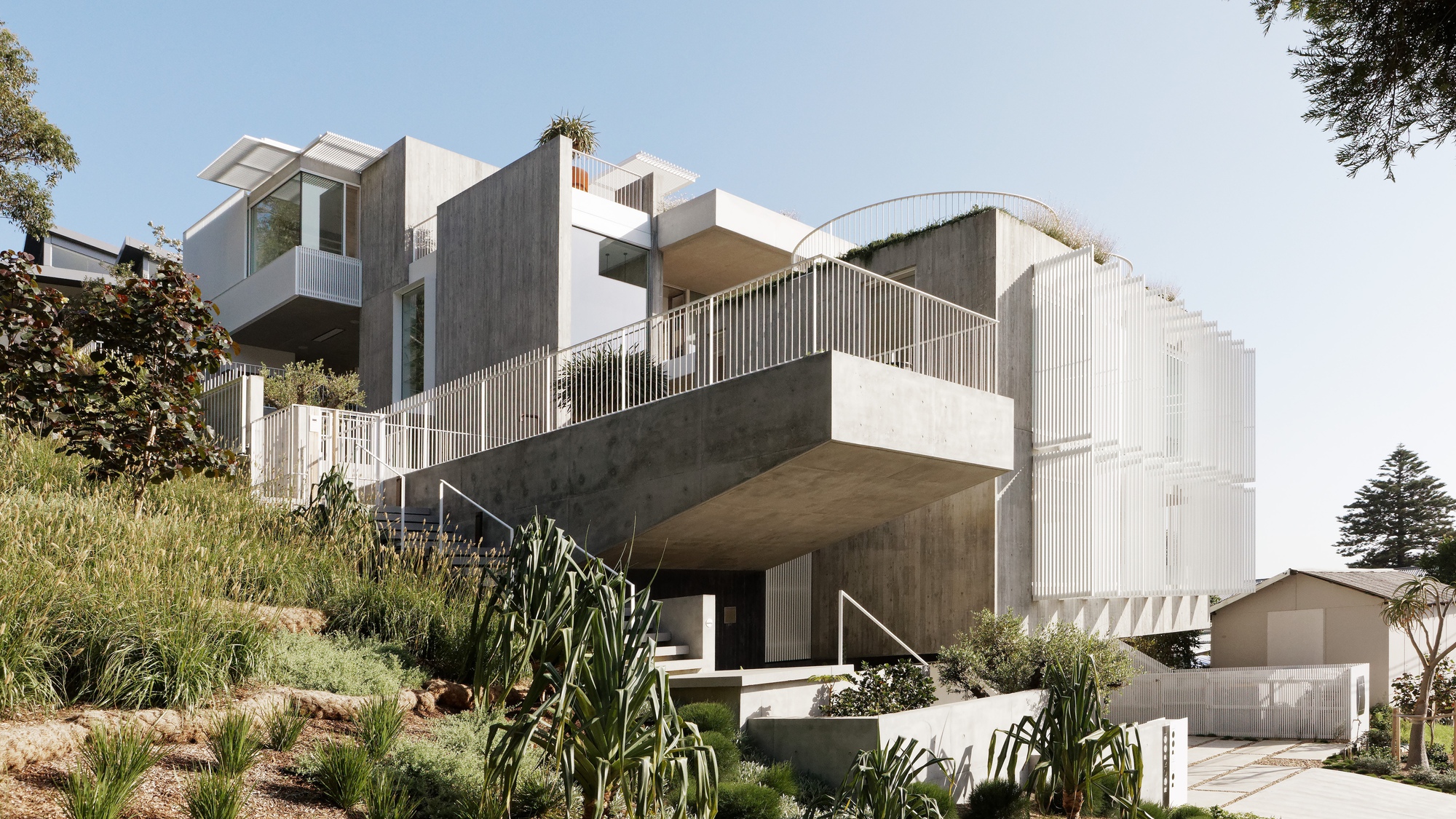 Lower view of the terraced concrete volumes with vertical white screening and native coastal planting