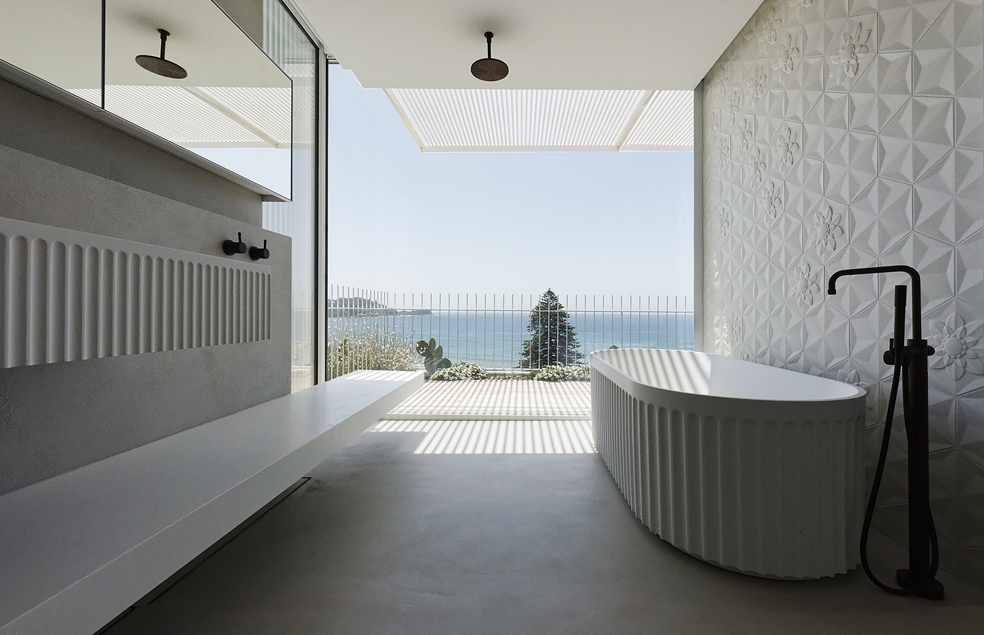 Bathroom with freestanding tub and textured tile wall opening to ocean view through corrugated screen