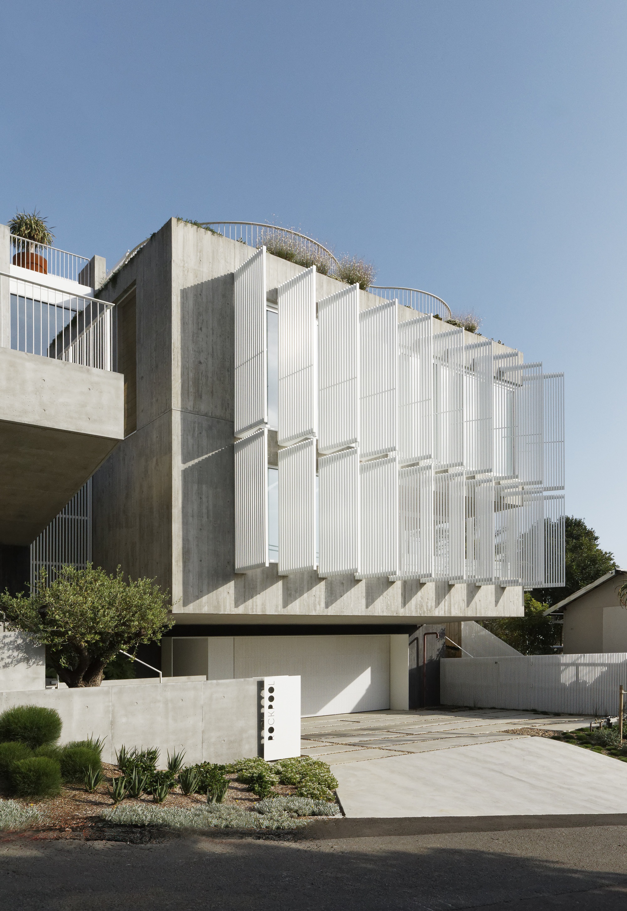 Side elevation showing the ribbed white facade stepping back above exposed concrete cores and planter boxes