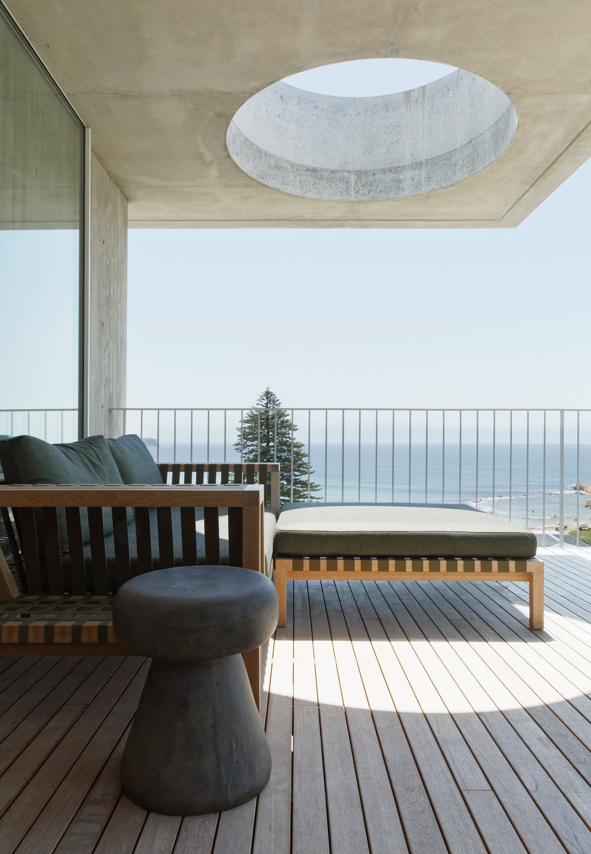 Outdoor terrace with timber furniture and circular skylight cut into the concrete soffit above