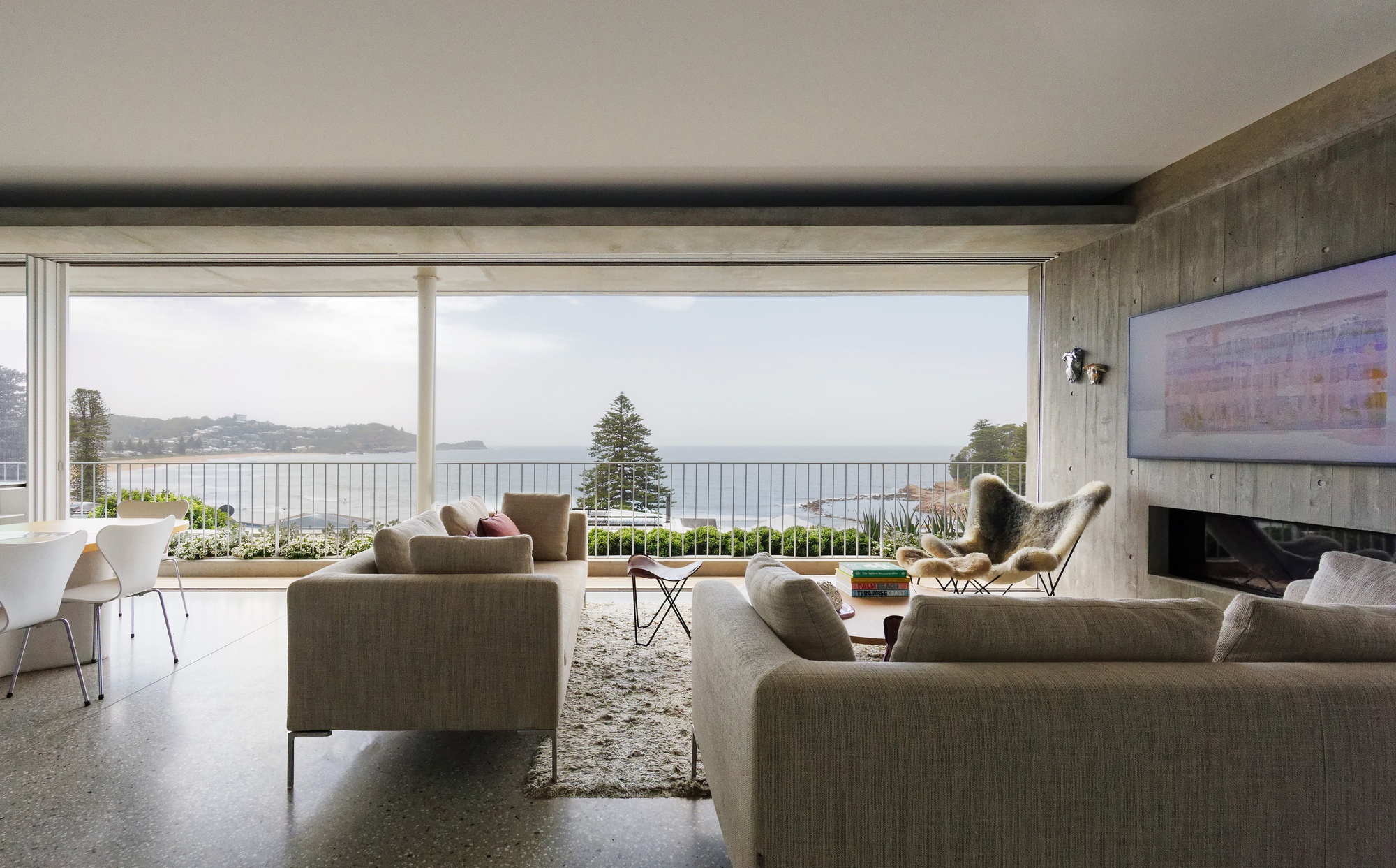 Living room with polished concrete floor and full-height glazing framing coastal views