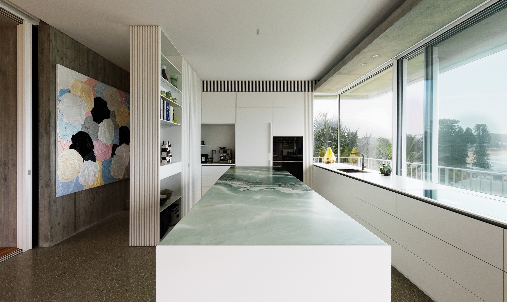 Kitchen with green veined stone island and white cabinetry stretching toward the glazed corner