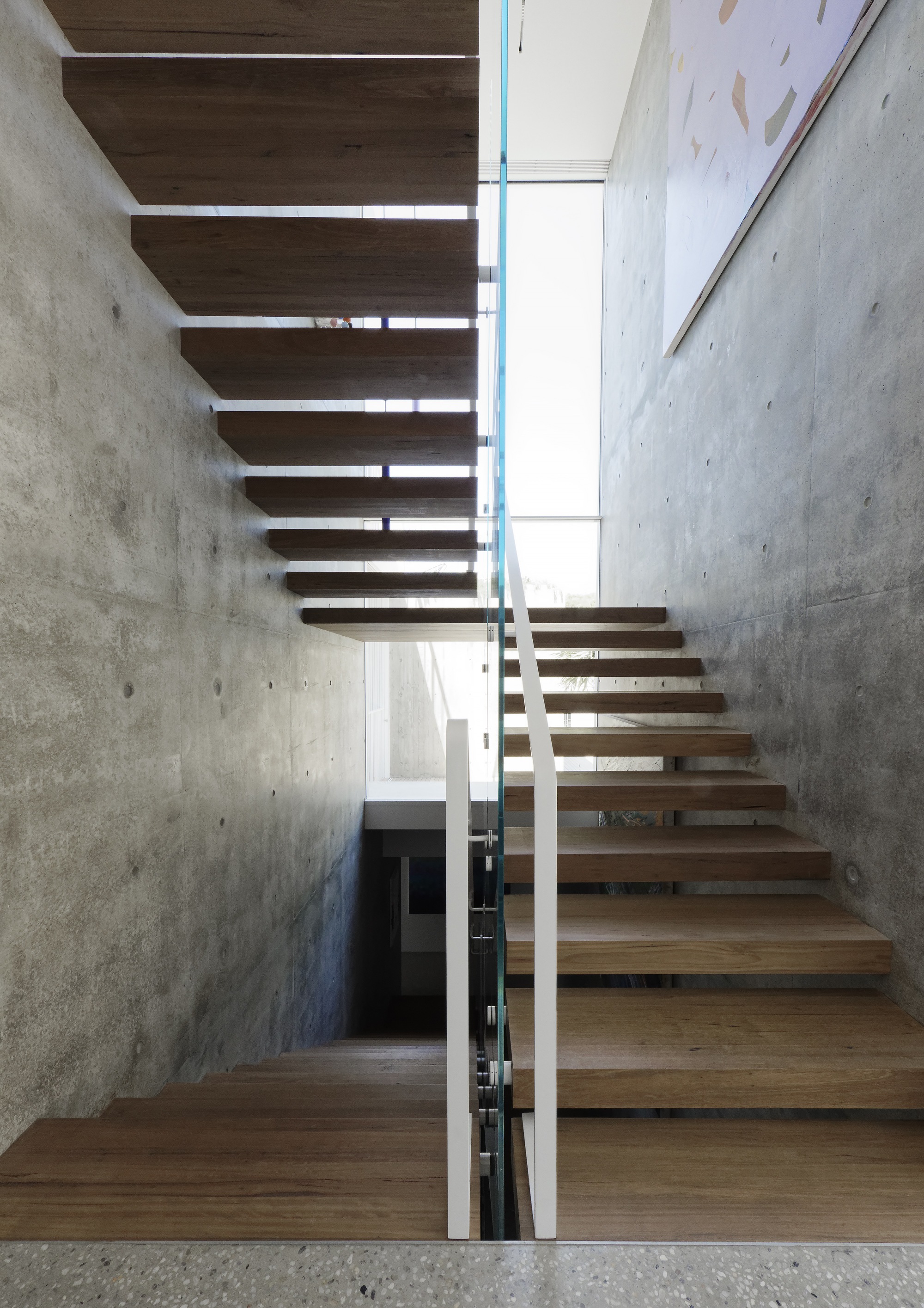 Timber staircase with open treads ascending between board-formed concrete walls and glass balustrade