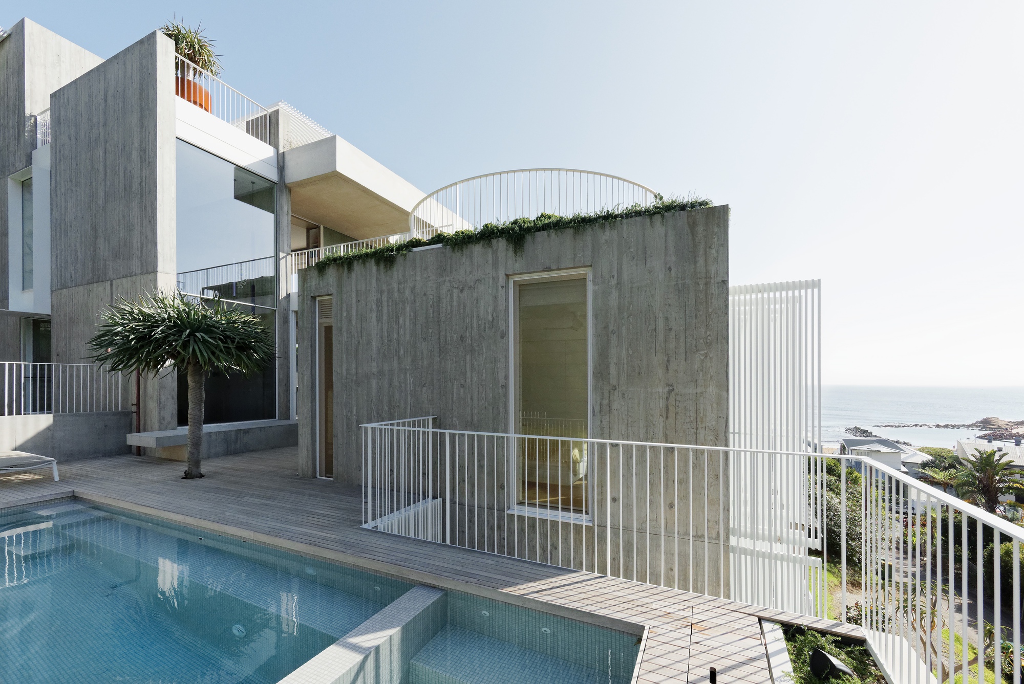 Pool deck with curved concrete pavilion and white metal railings overlooking the coastline