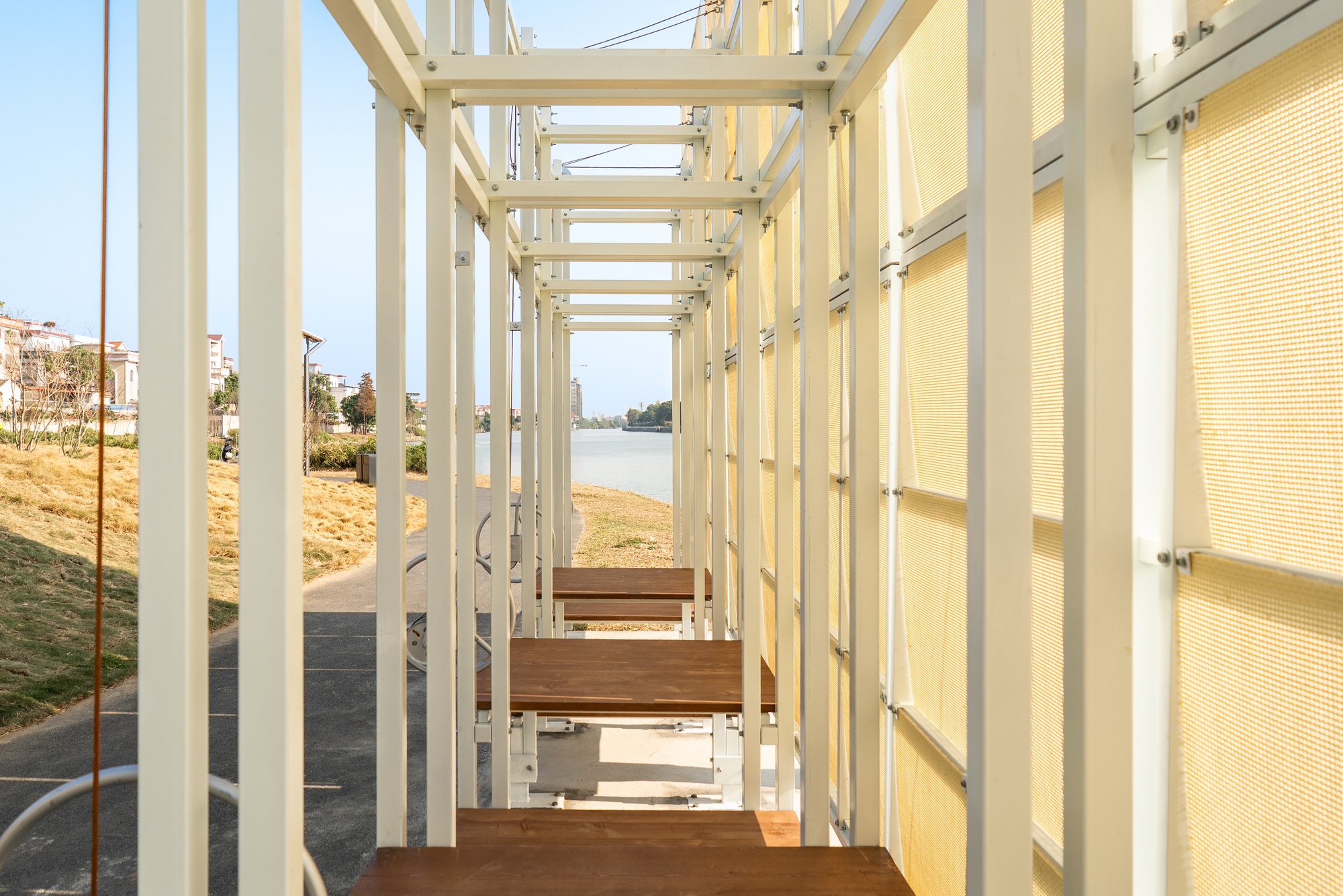 Interior view through white steel columns and timber benches framing the river beyond