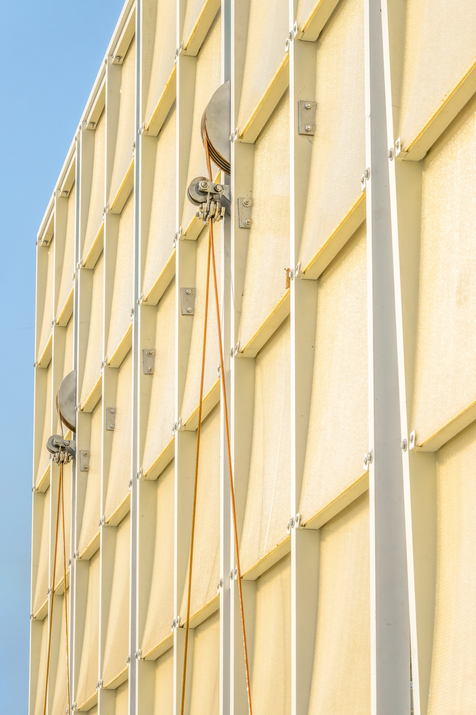 Close-up of the vertical yellow fabric panels with metal clips and cables against blue sky