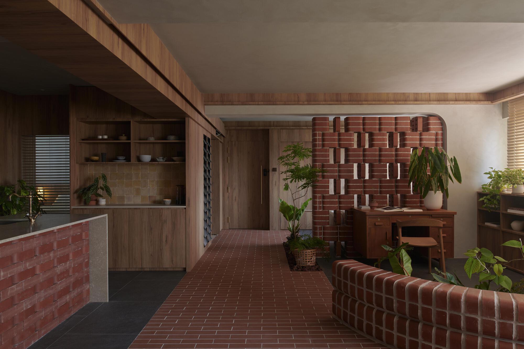 Open-plan living space with patterned red brick divider walls and timber joinery under soft ambient light