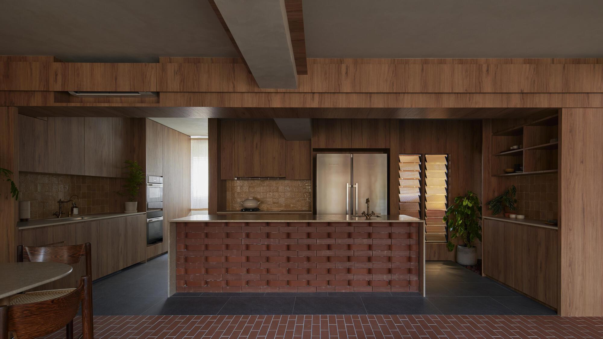 Kitchen island clad in checkered red brick tile beneath timber cabinetry and angled ceiling