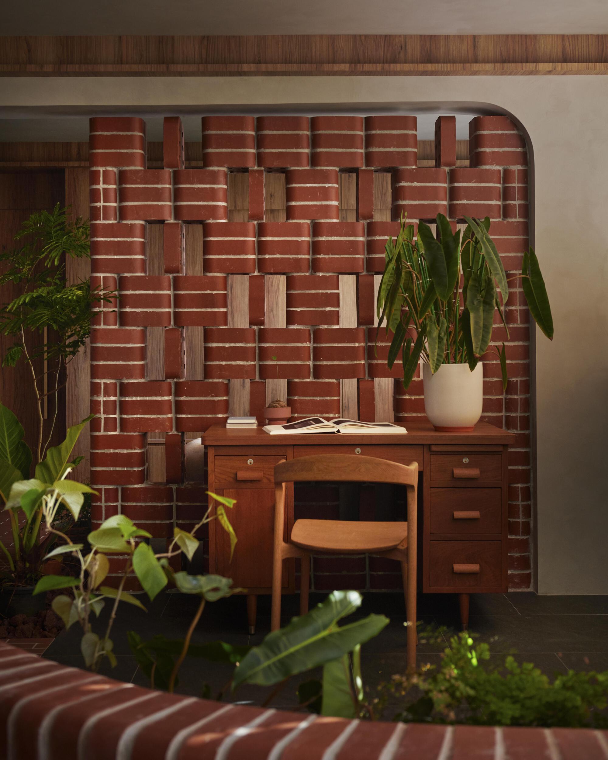 Timber desk tucked into a woven brick and wood niche alcove surrounded by leafy potted plants