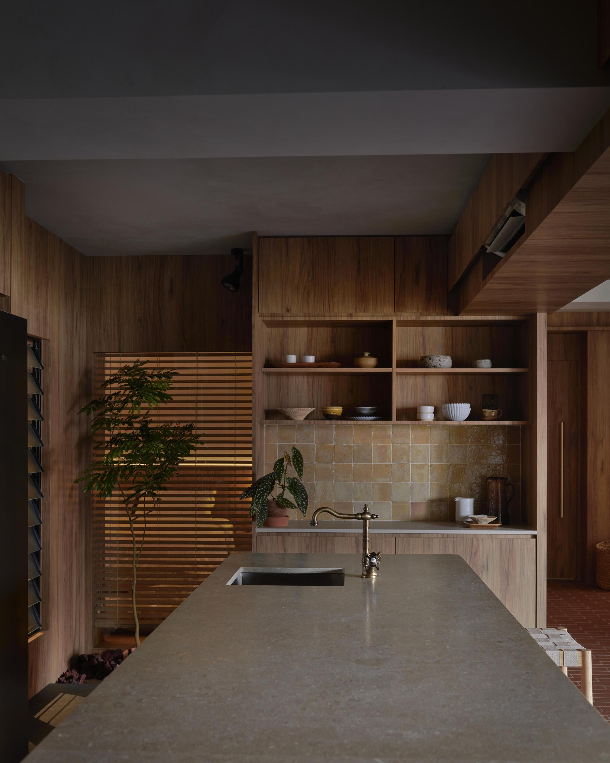 Concrete kitchen counter with horizontal timber louver screen filtering daylight beside open shelving