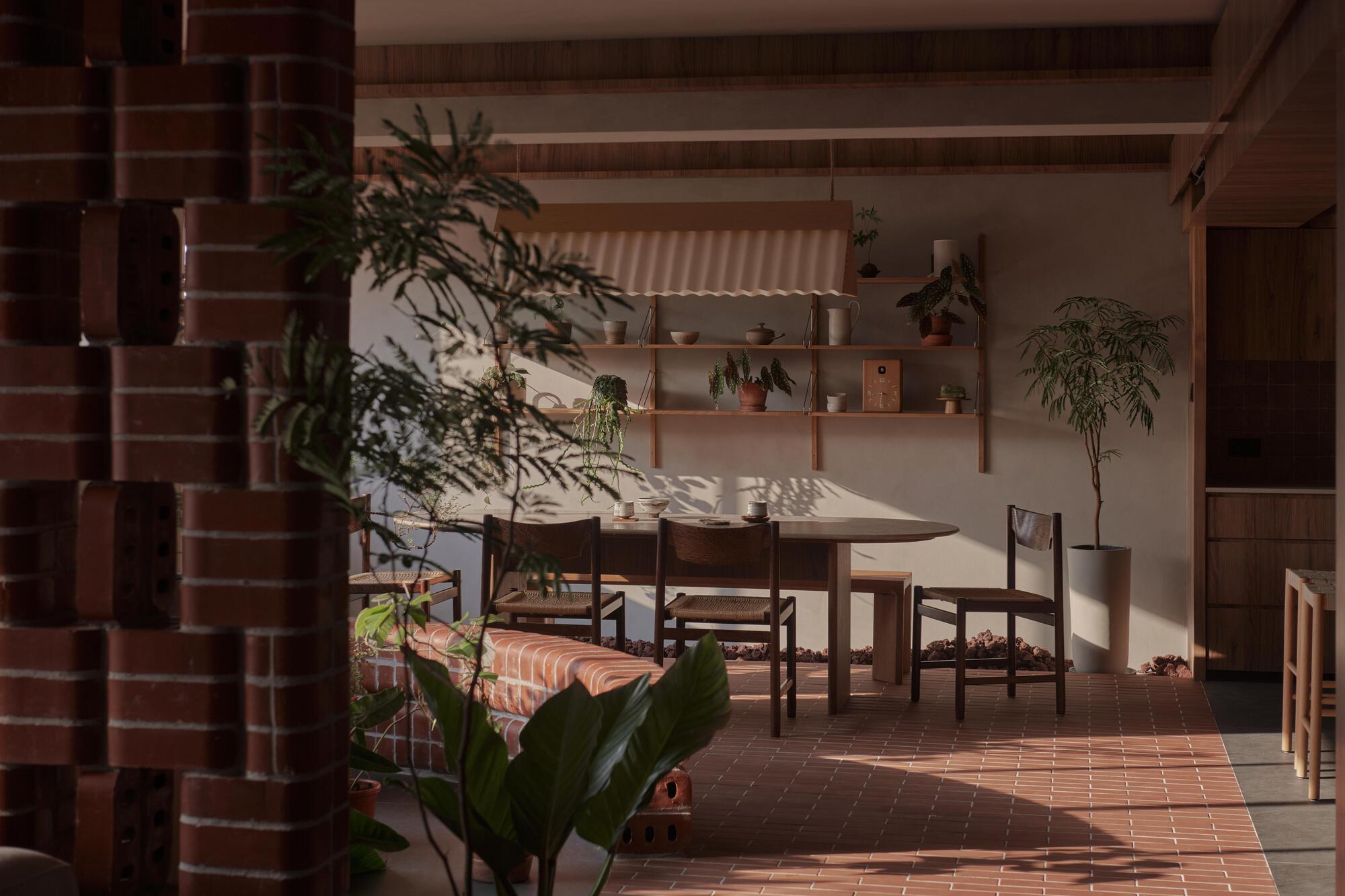 Dining area with brick tile floor and freestanding plants in afternoon sunlight filtering through screens