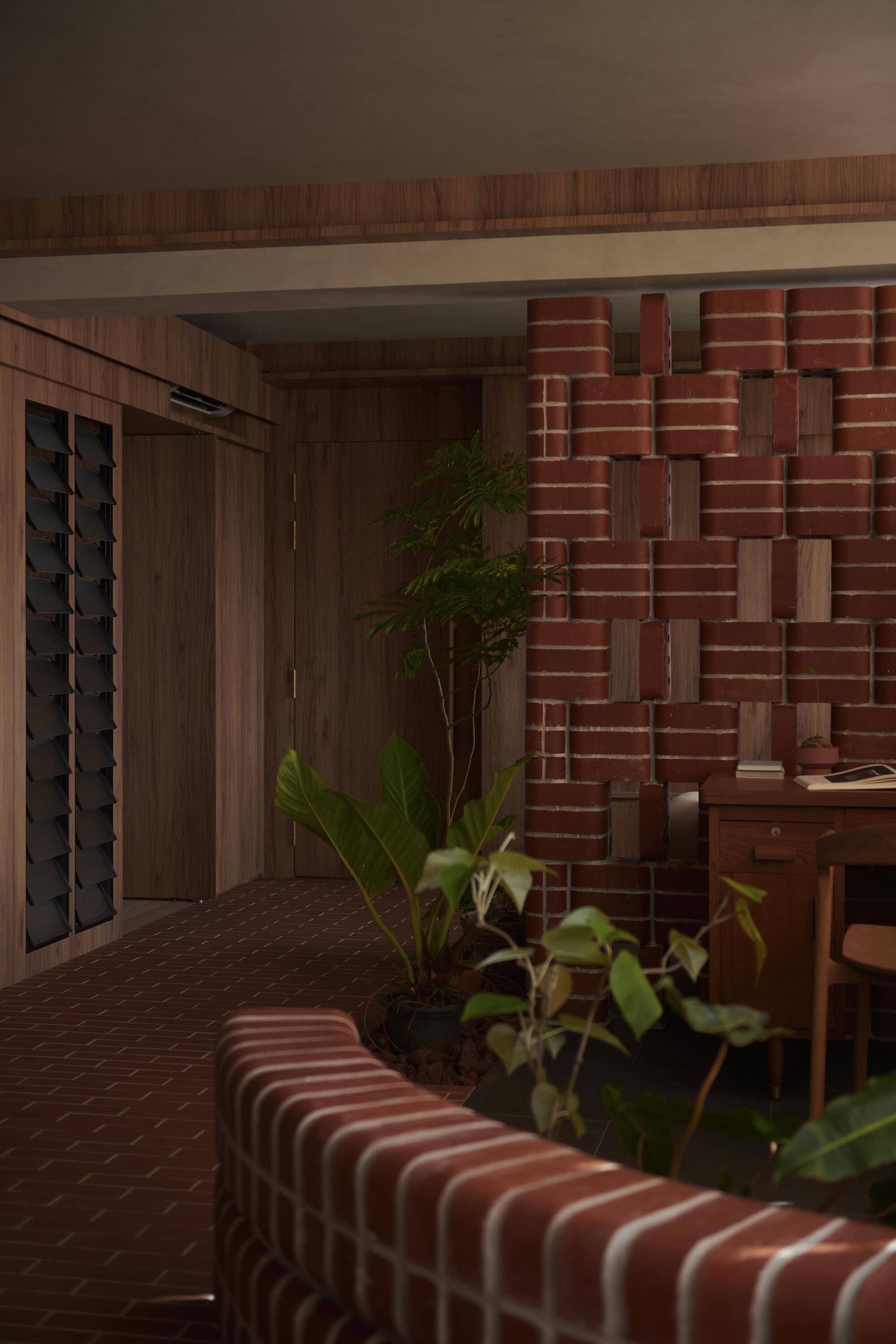 Layered red brick wall forming an undulating relief surface beside planted greenery