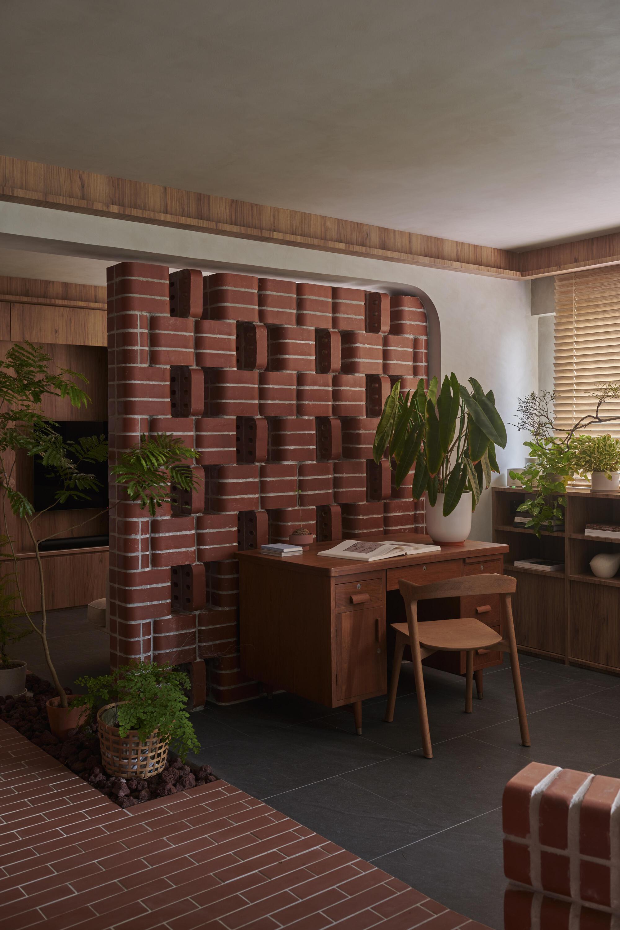 Sculptural red brick wall with protruding blocks behind a timber desk and potted plants