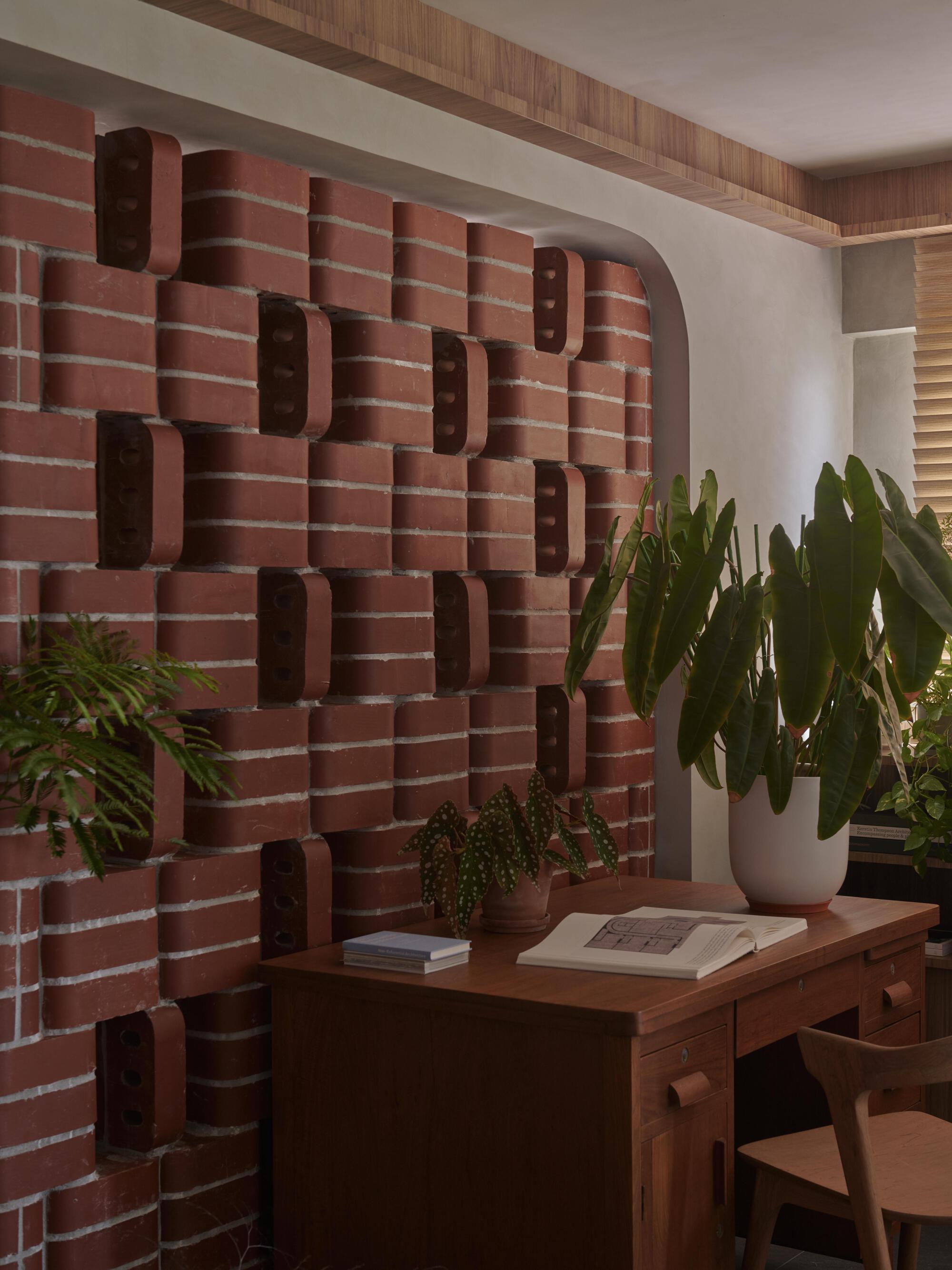 Close-up of the textured brick wall with recessed slots beside a desk with plants