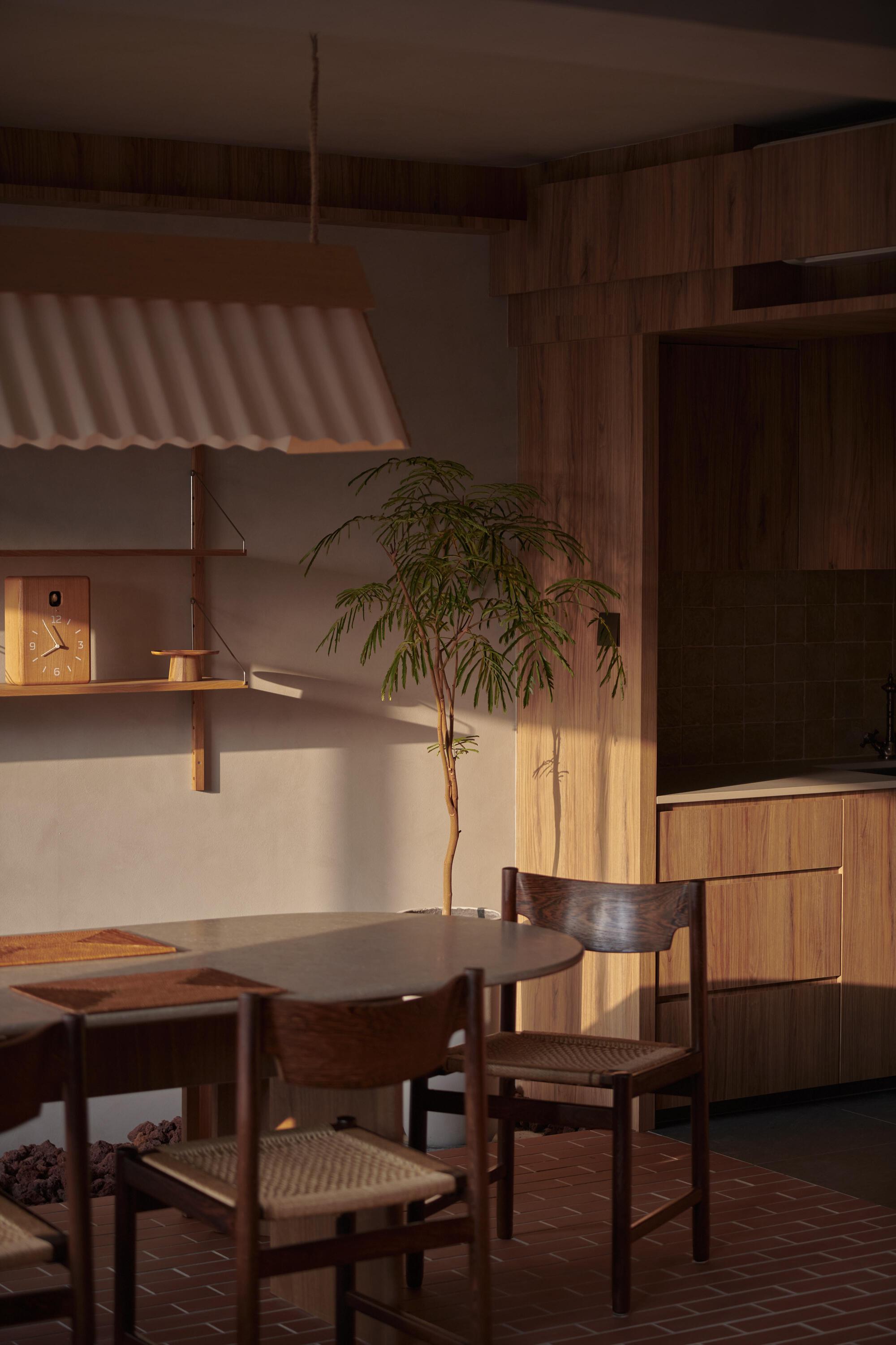 Dining table with woven-seat chairs beneath a corrugated pendant lamp at dusk