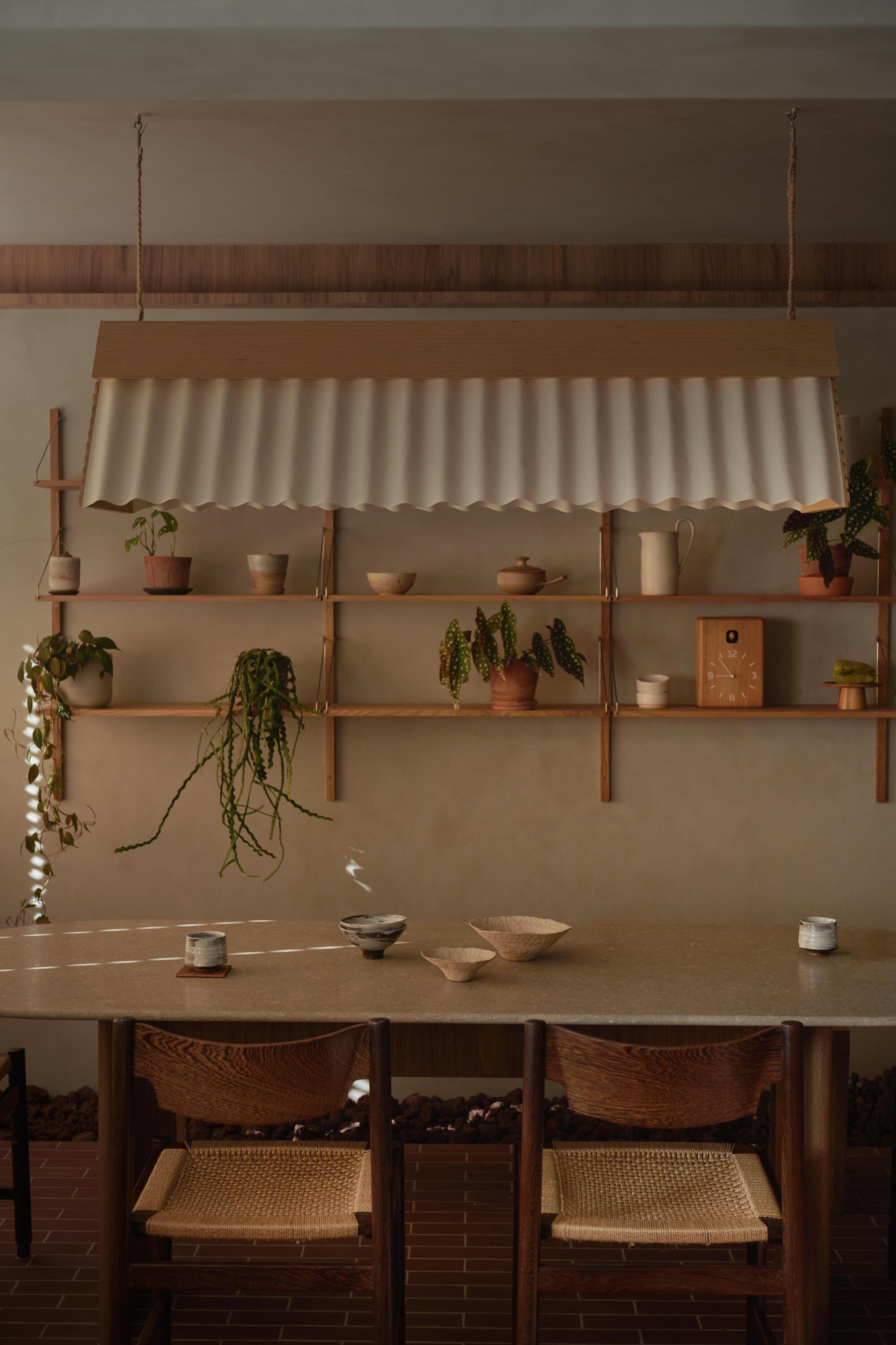 Dining area with wall-mounted timber shelves displaying potted plants beneath a suspended corrugated canopy