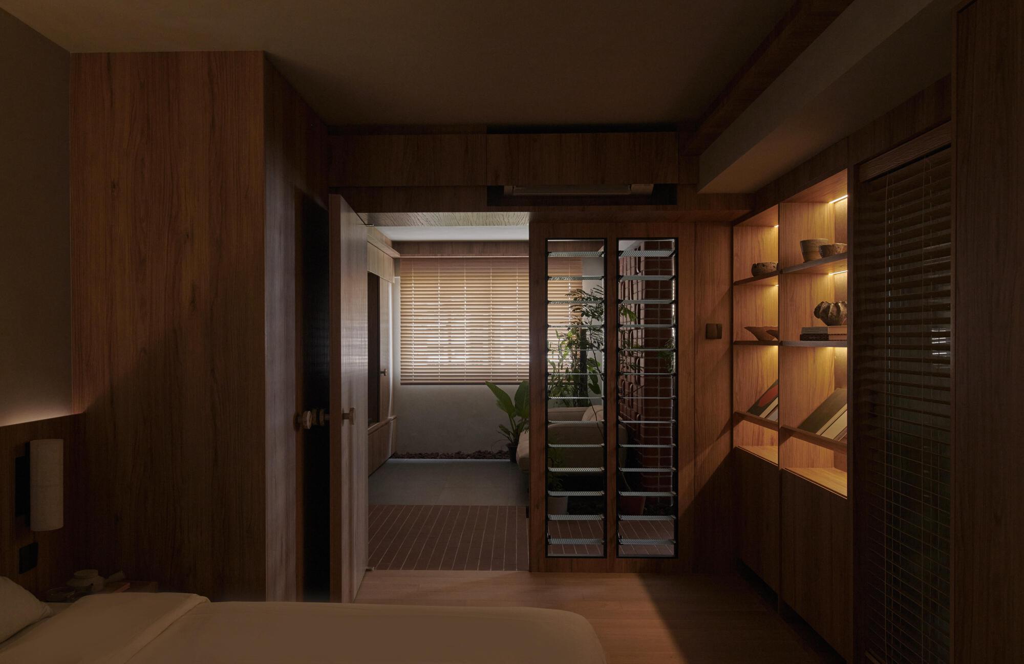 View through timber-paneled bedroom toward corridor with horizontal blinds and built-in shelving