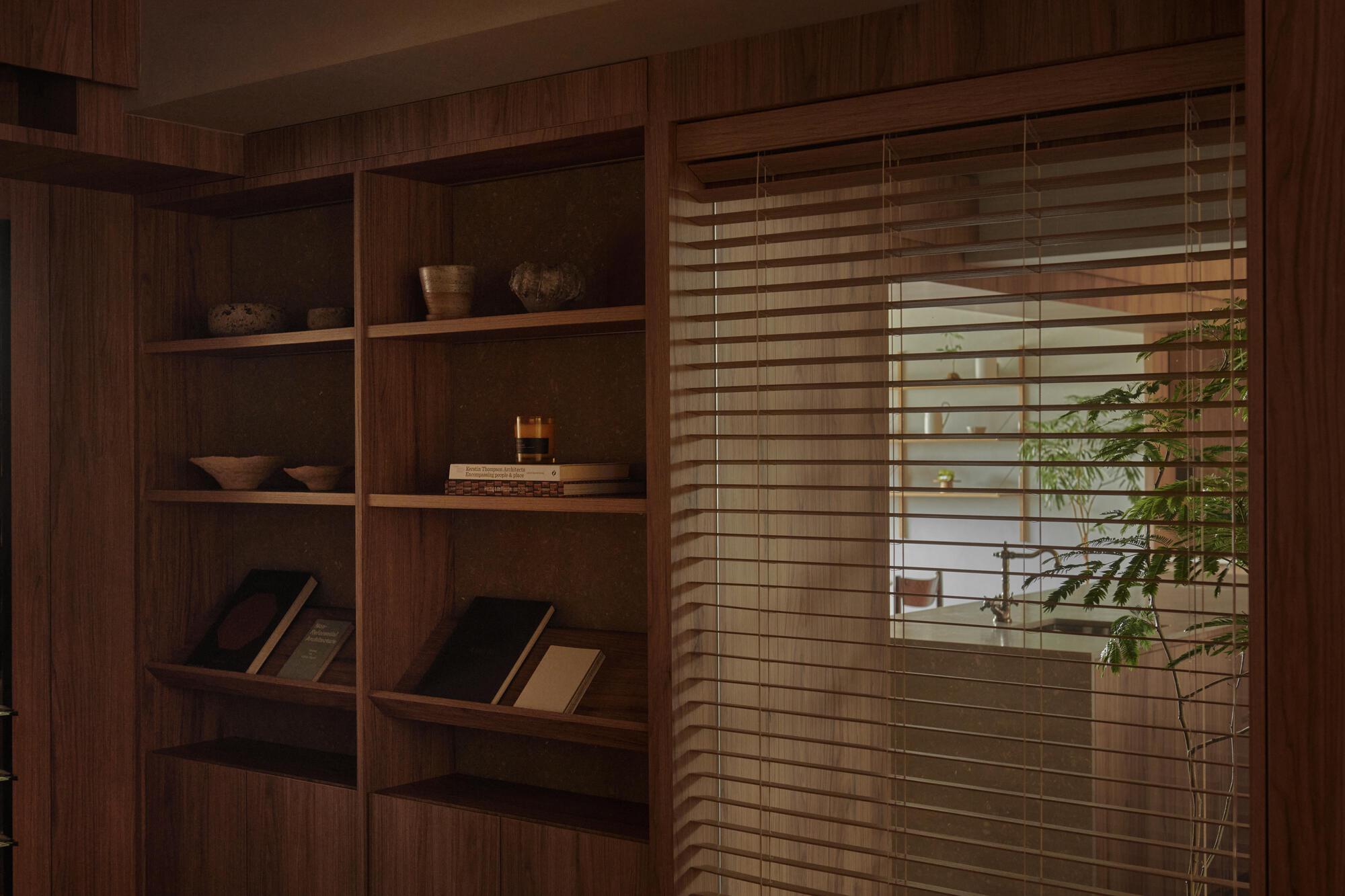 Timber bookshelf beside horizontal timber blinds screening a planted balcony beyond