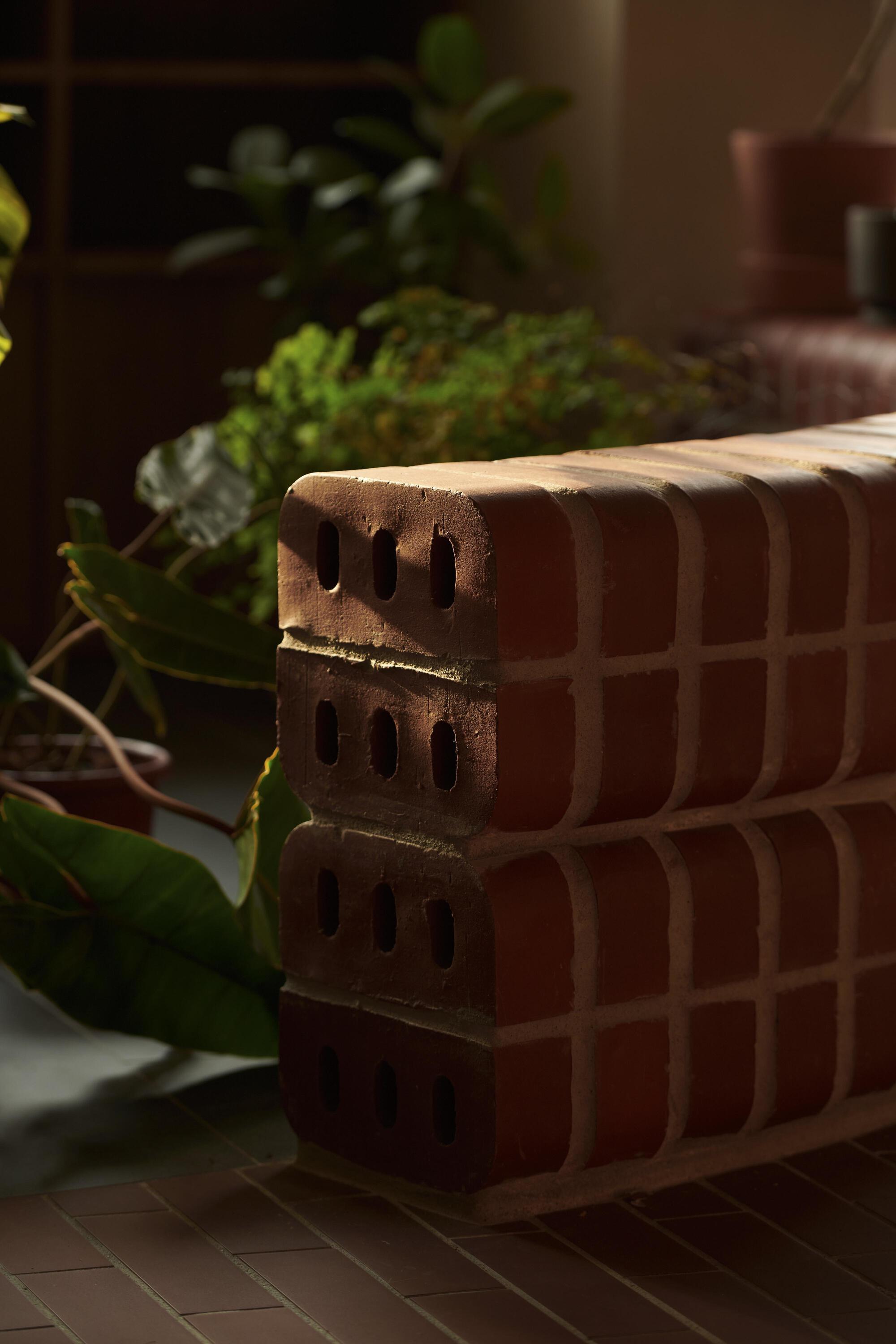 Close-up of terracotta brick stack with perforations beside potted greenery in dappled sunlight