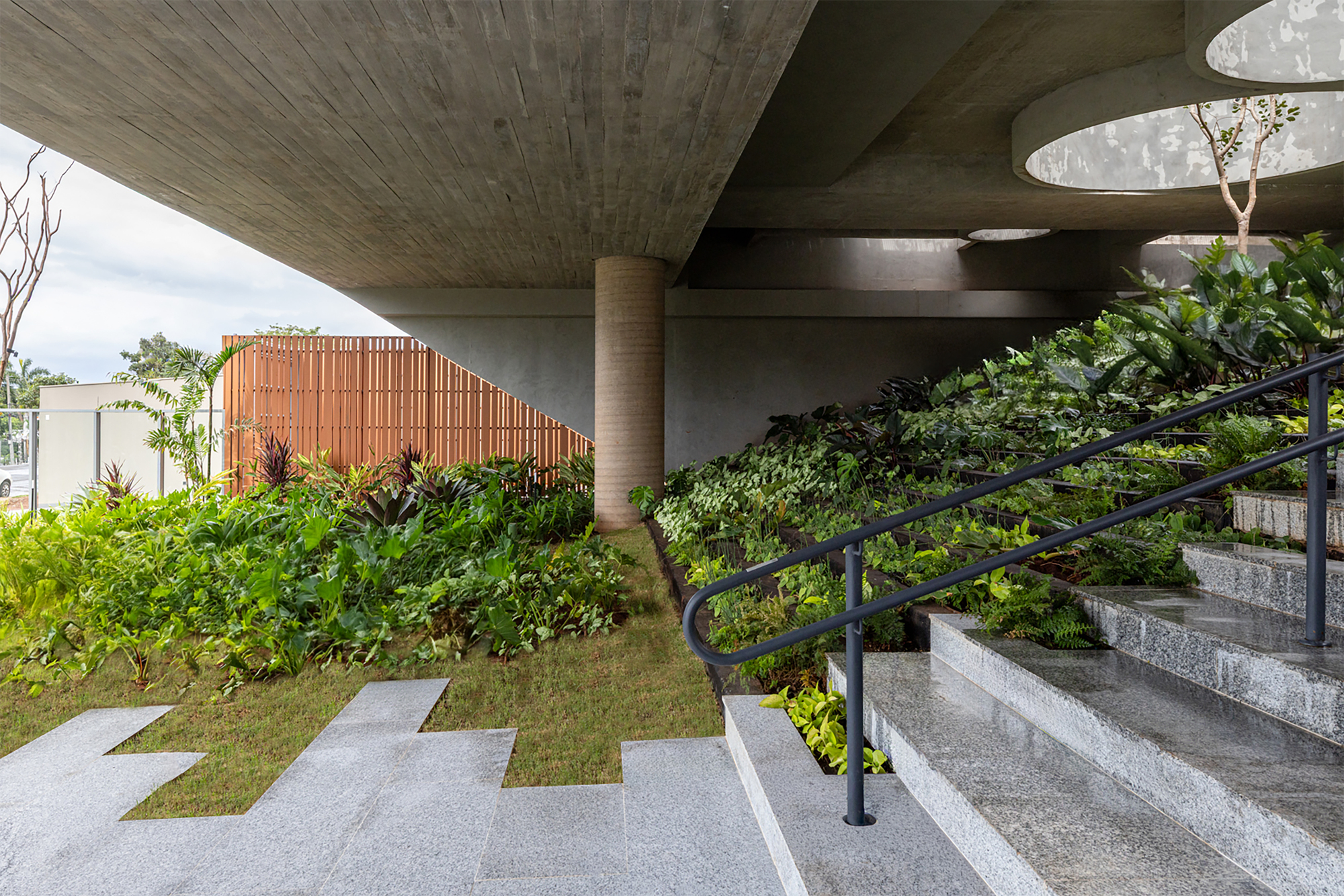 Covered entry with board-formed concrete ceiling, planted terraces and granite steps with black handrail