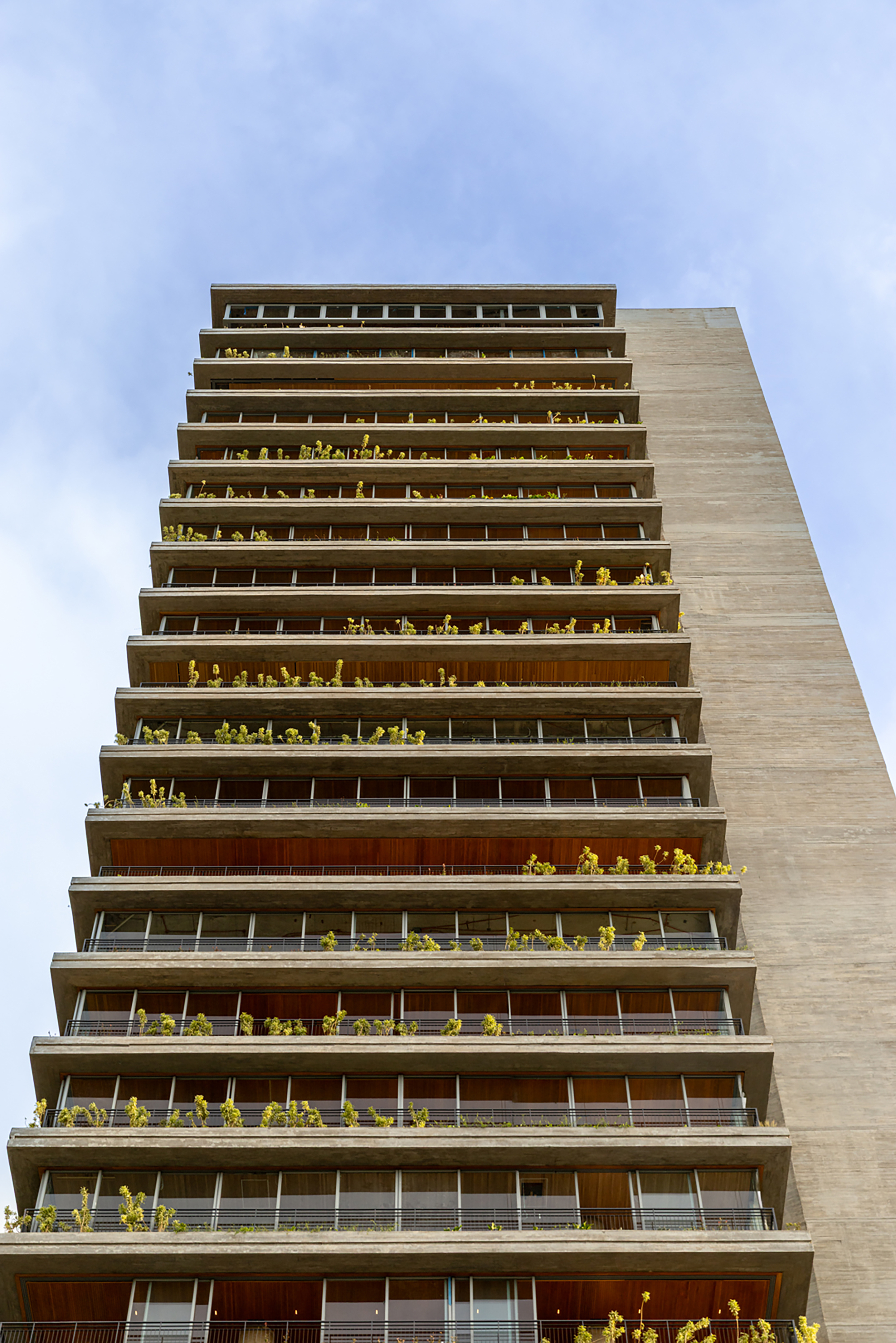 Tower facade with stacked balconies featuring glass railings, timber panels, and greenery on every level