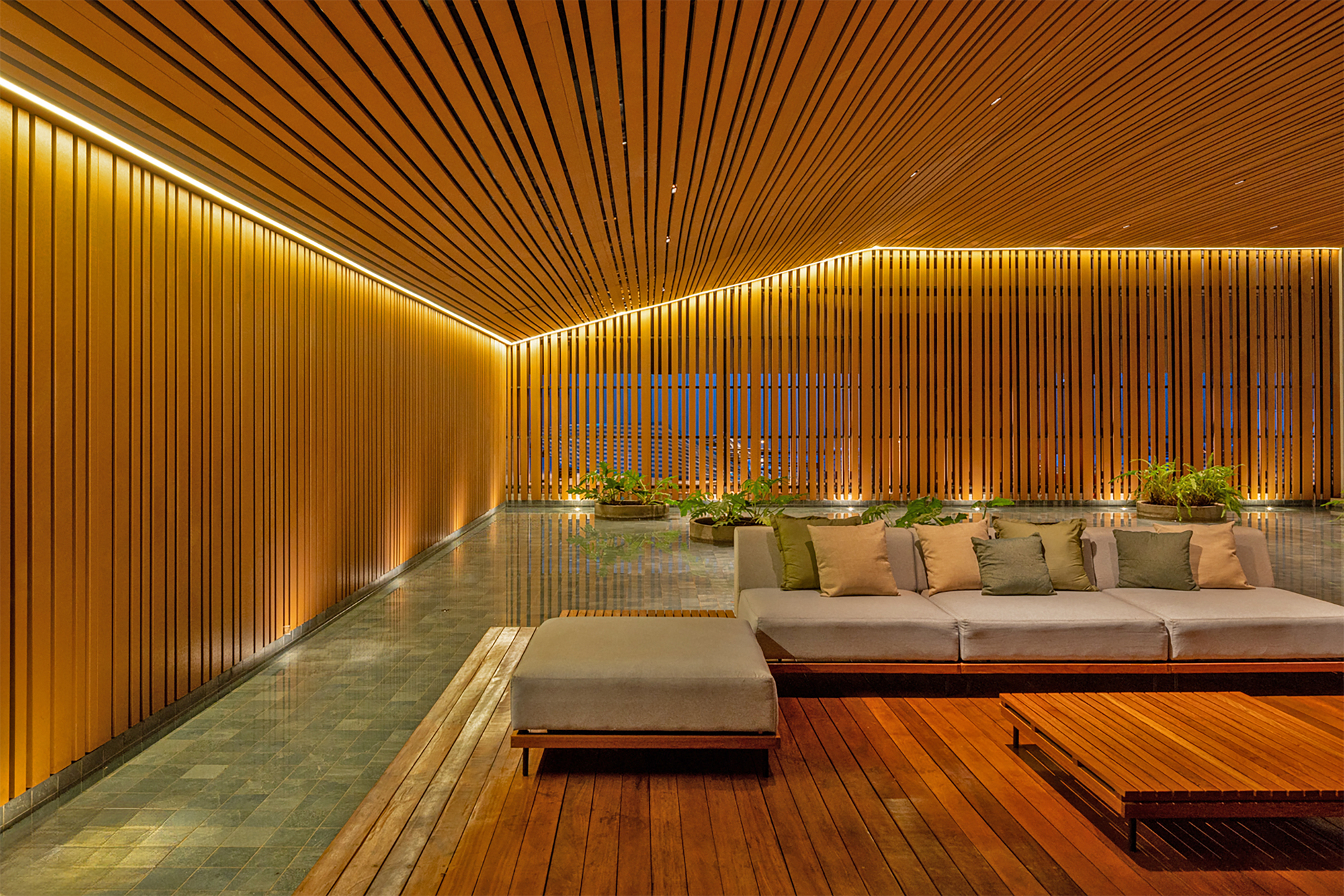 Corner lounge with upholstered sectional on wood platform framed by illuminated vertical wood slats and overhead baffles
