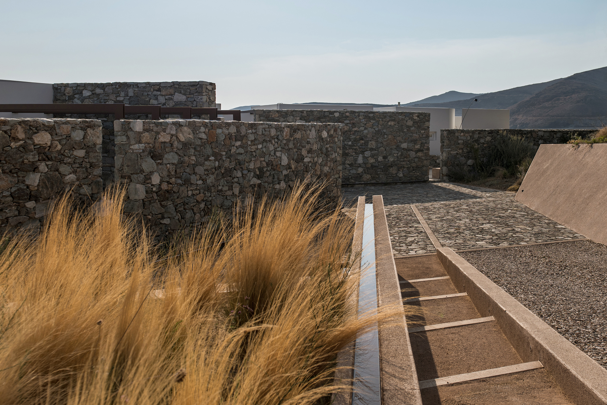Linear water channel beside dry grasses leading toward stone walls and distant hills