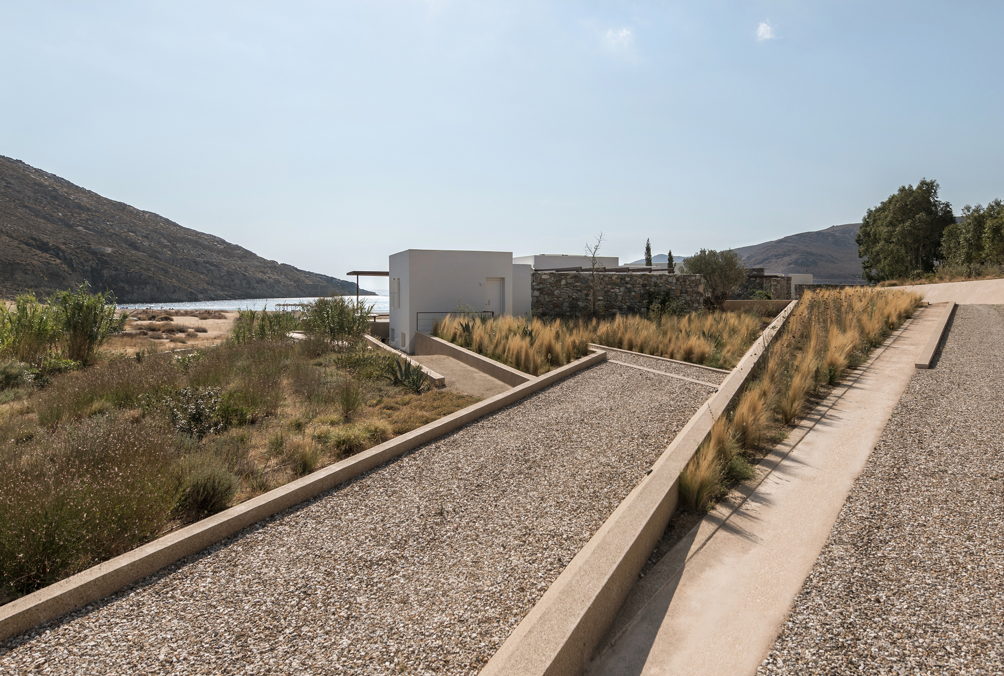 Stepped concrete pathway with gravel fill and ornamental grasses leading toward white volumes and distant hills