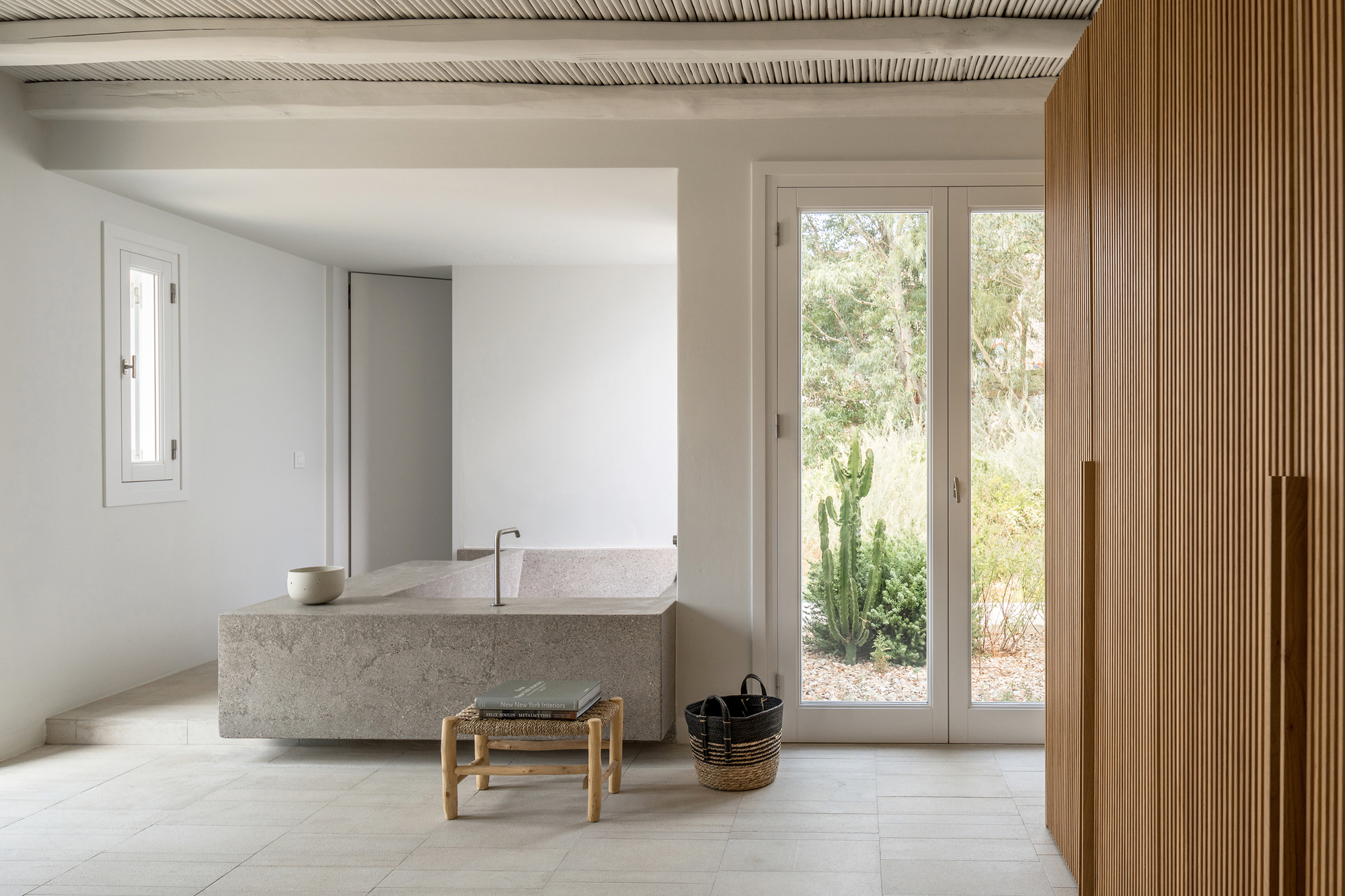 Bathroom with freestanding terrazzo tub, exposed timber ceiling beams, and glazed doors to planted courtyard