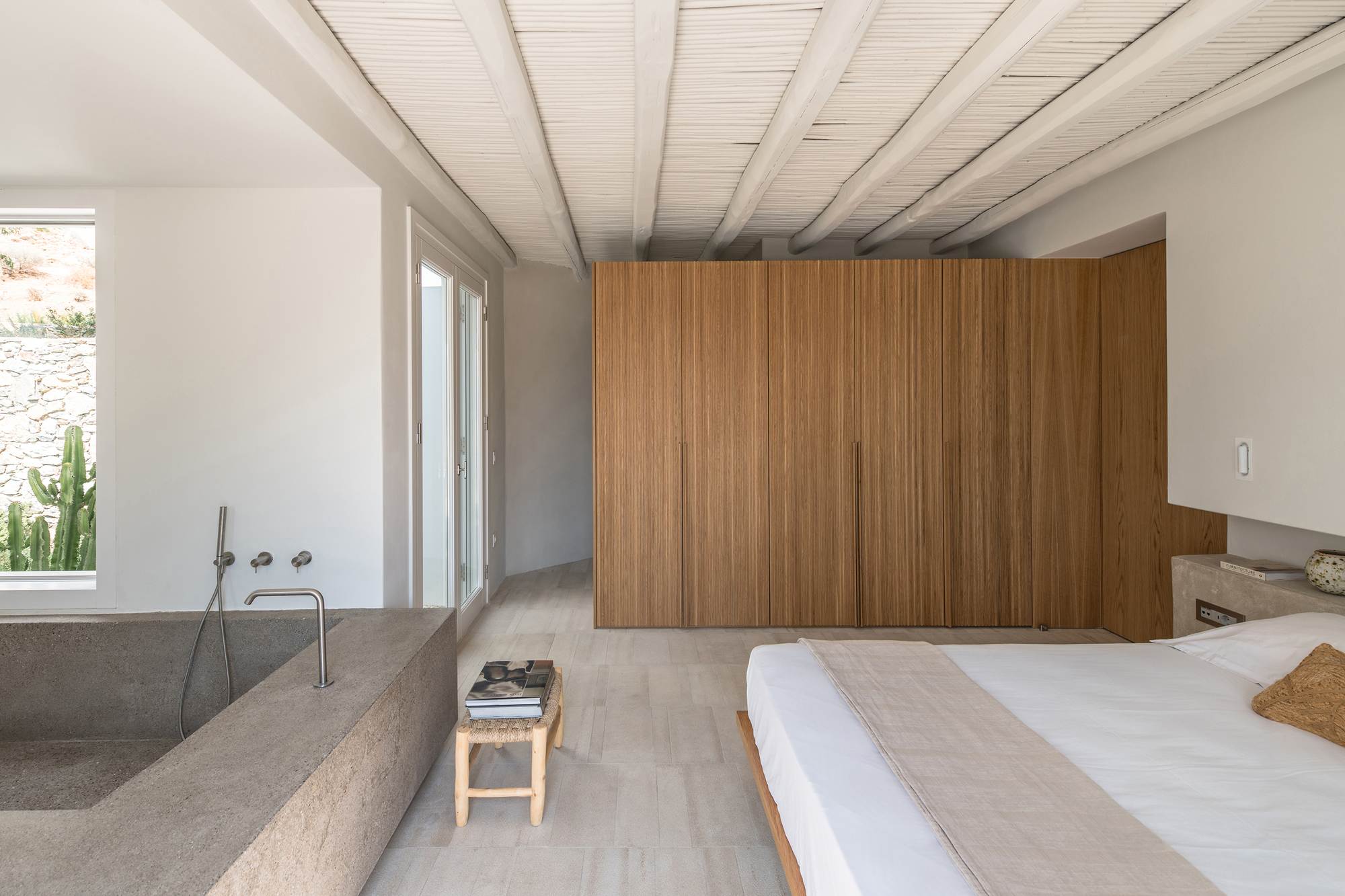 Bedroom with integrated terrazzo bathtub, vertical timber slat wall, and exposed beam ceiling in daylight